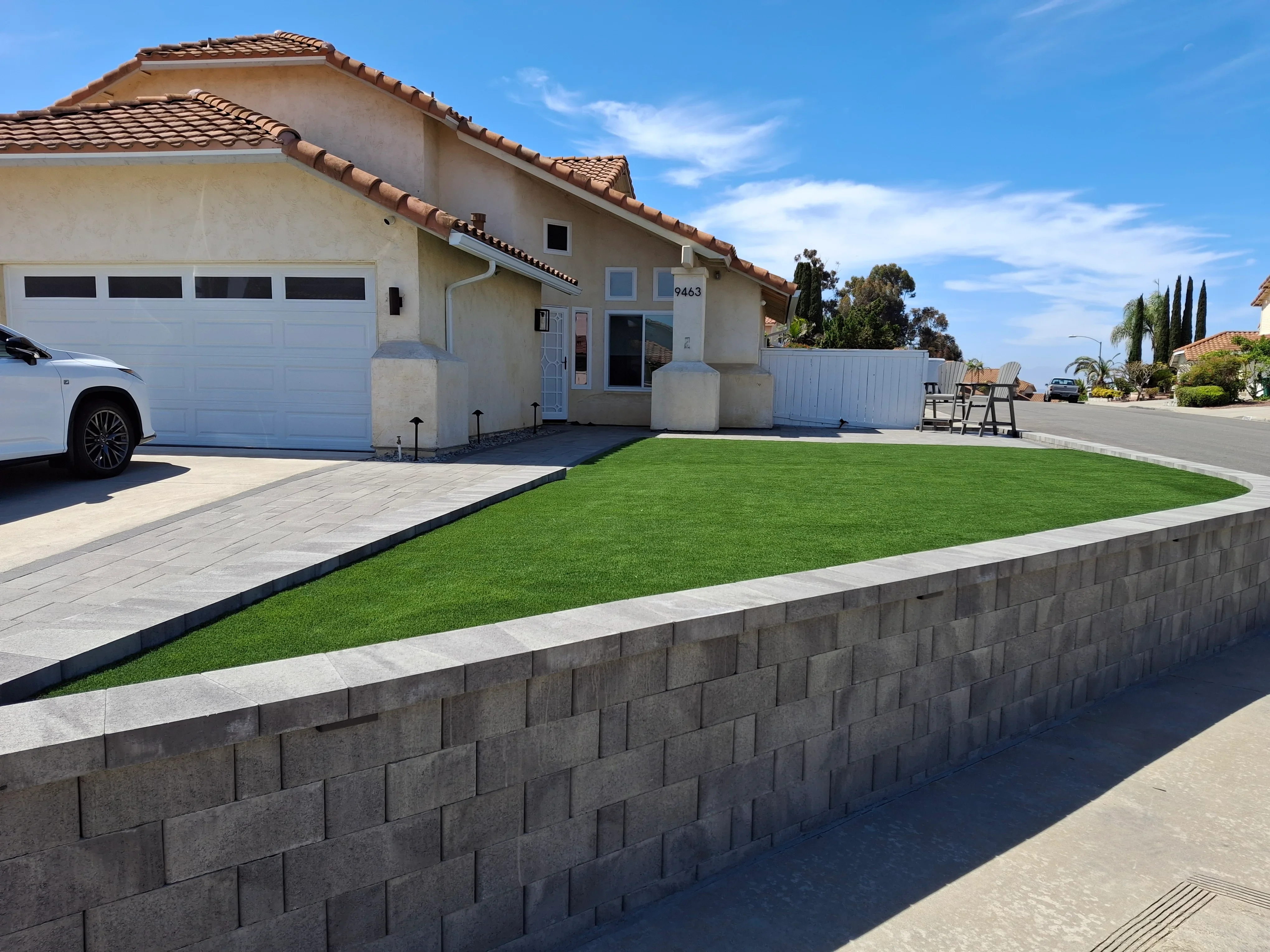 Concrete retaining wall, sod lawn, and paver driveway with metal edging in front yard