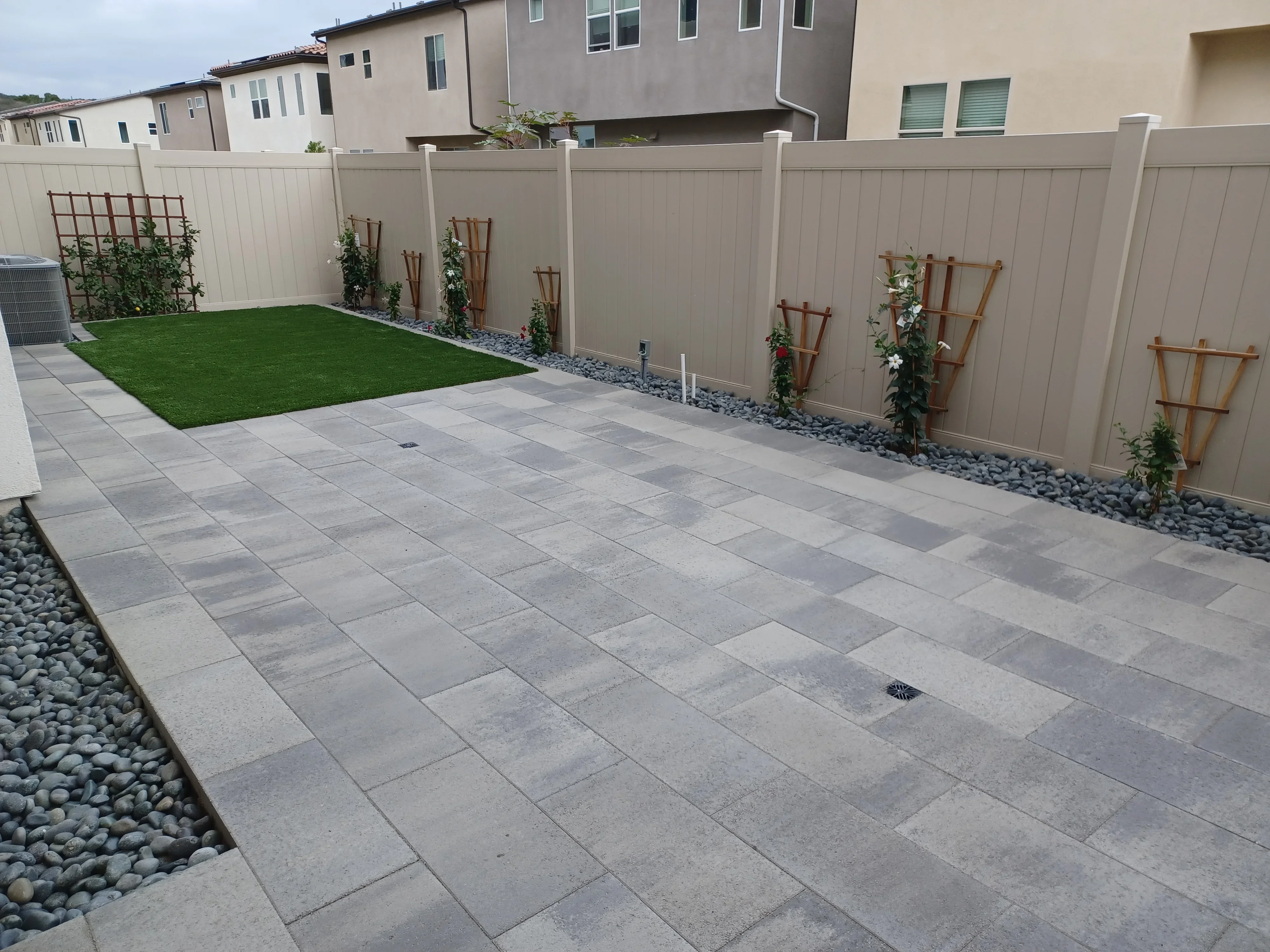 Gray concrete paver patio with river rock borders, composite fence, and wooden trellises with climbing plants