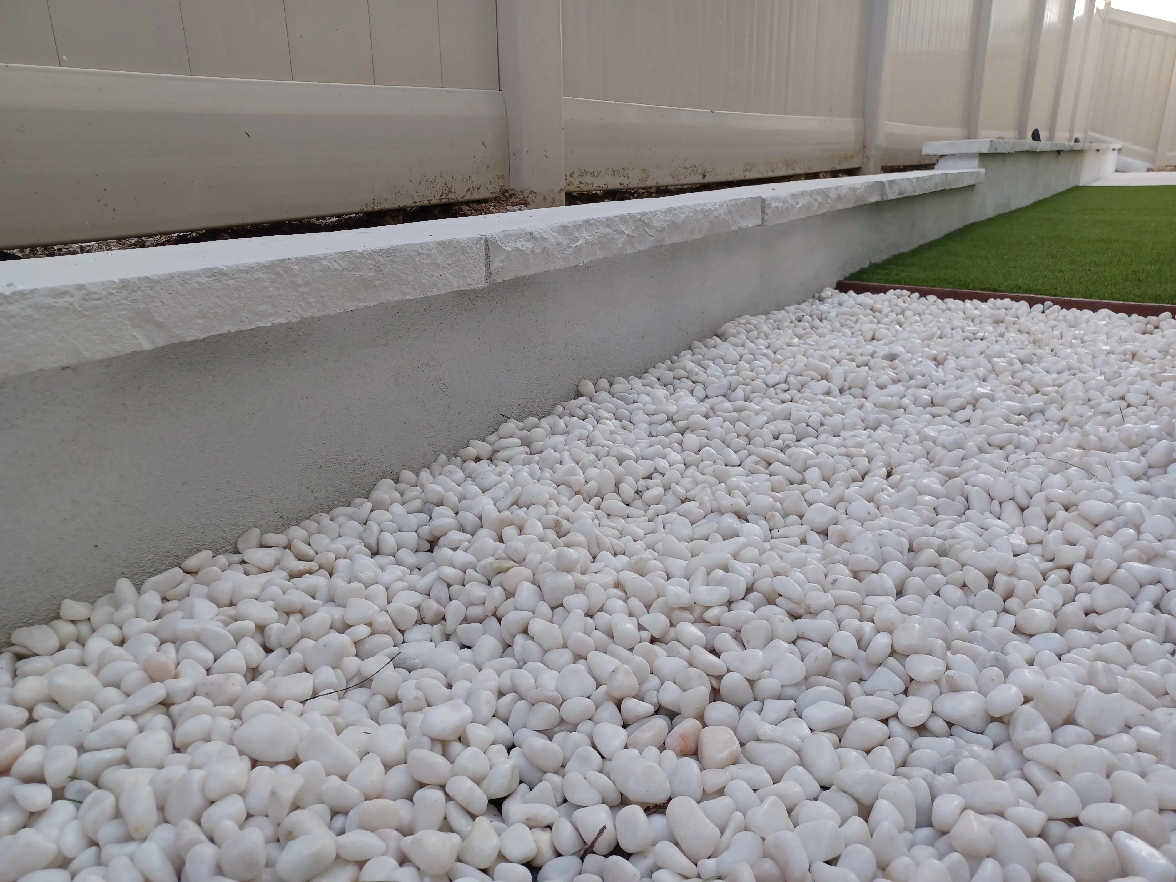 White river rock landscape bed with concrete retaining wall and textured cap edging