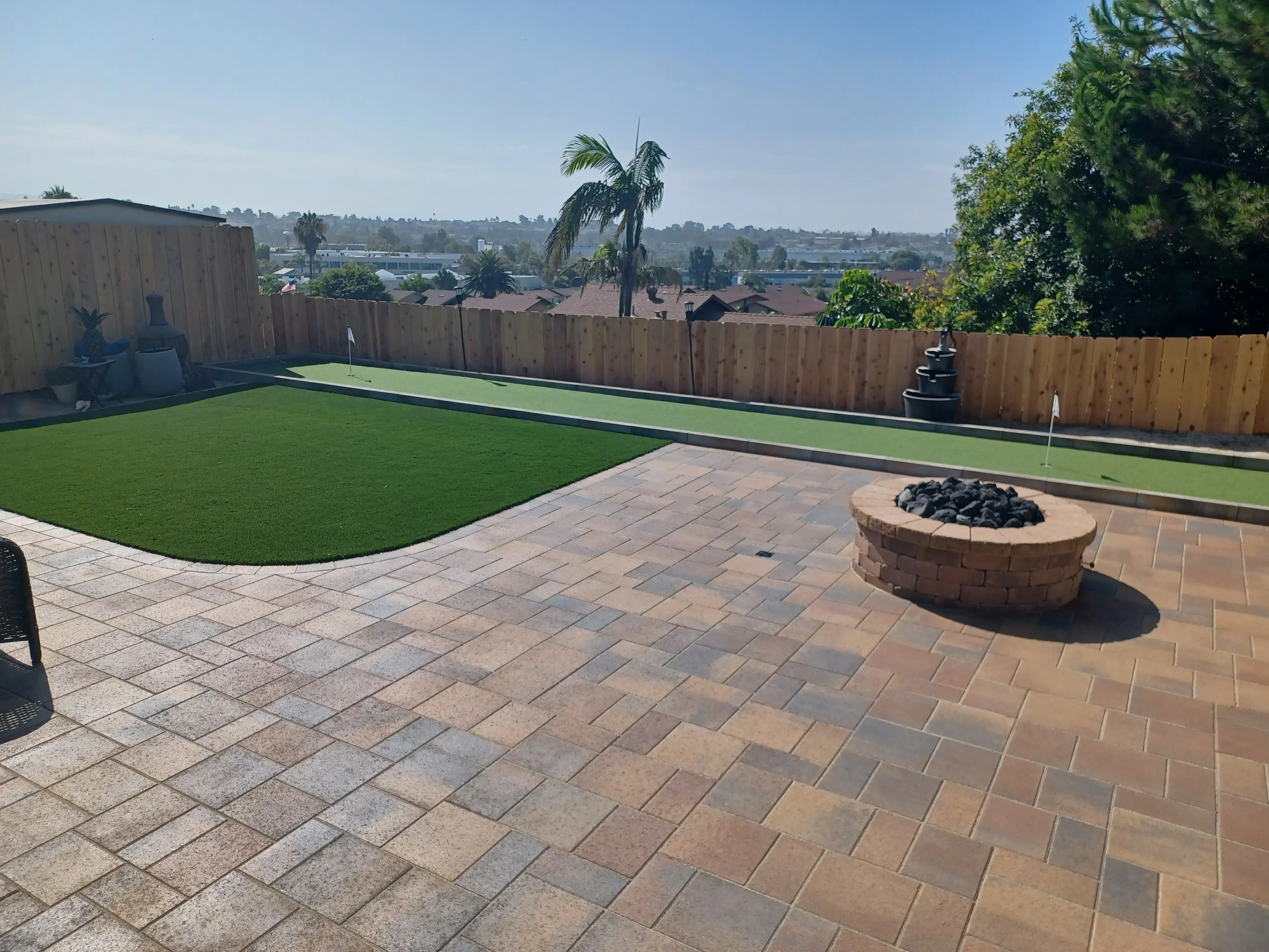 Paver patio with synthetic putting green, stone fire pit, and wood fence enclosure