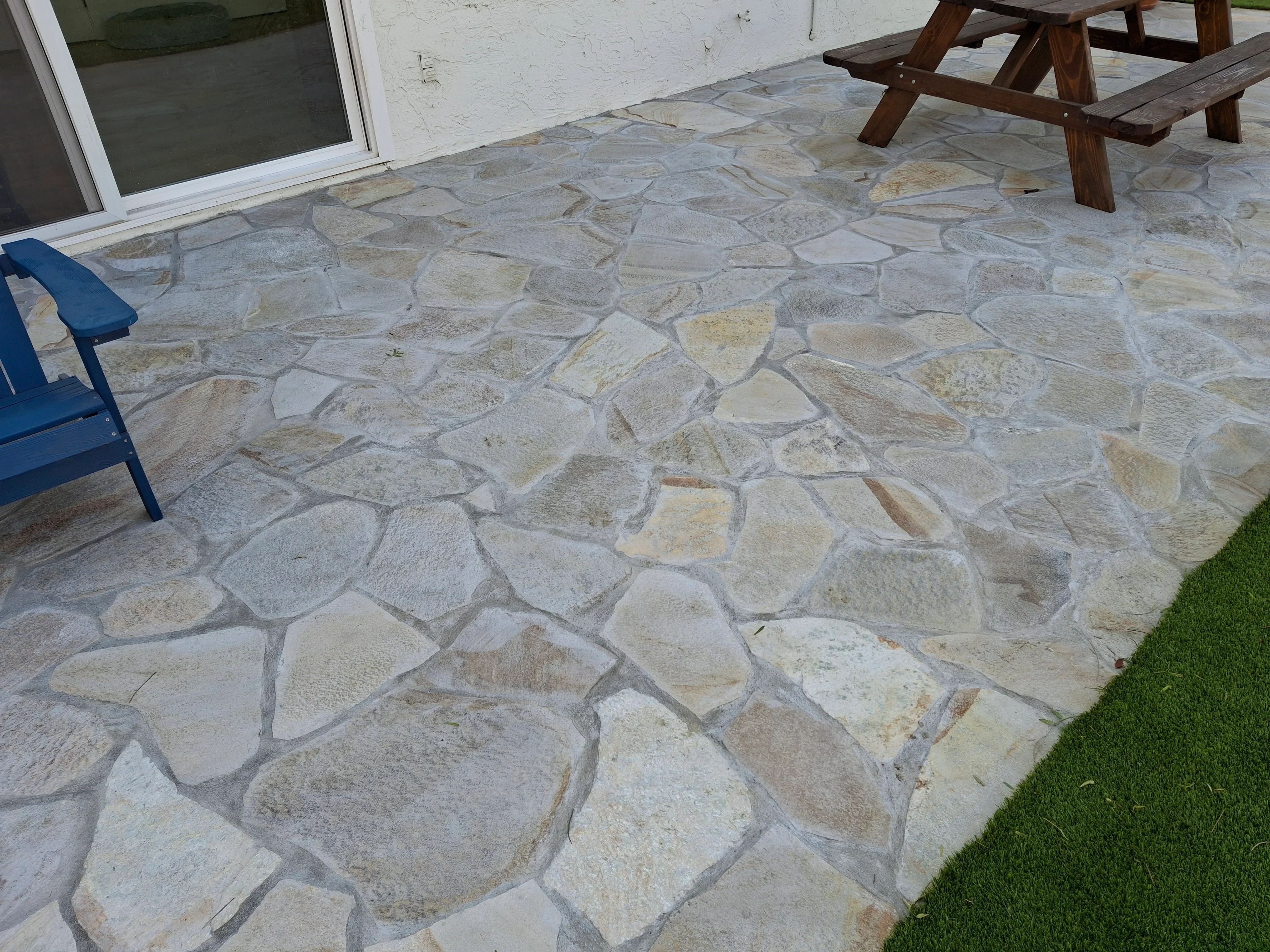 Irregular flagstone patio with cream and tan stones, mortared joints, adjacent to white house and lawn