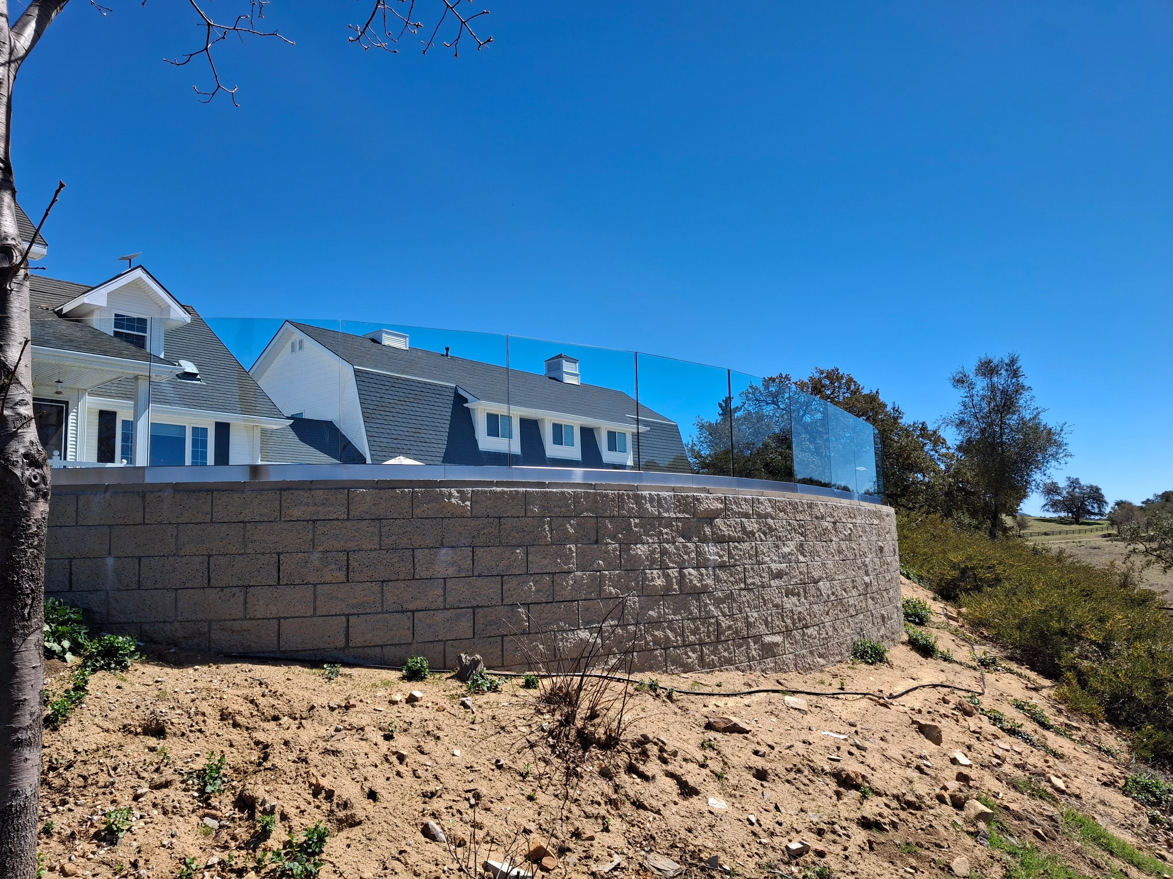 Textured concrete block retaining wall with glass railing system supporting residential home