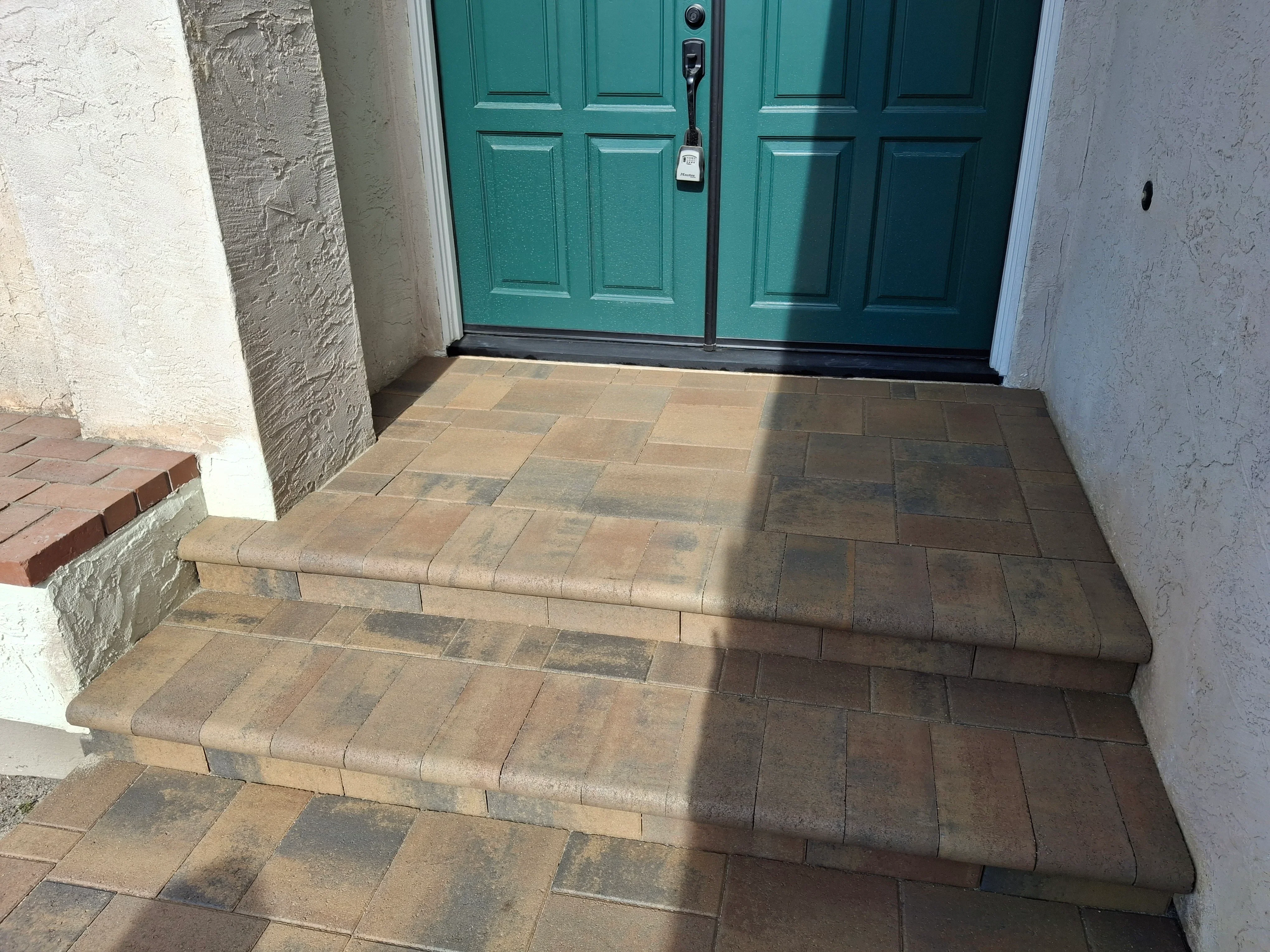 Multi-toned concrete paver entry stoop with stepped landing and bullnose edging leading to teal double doors