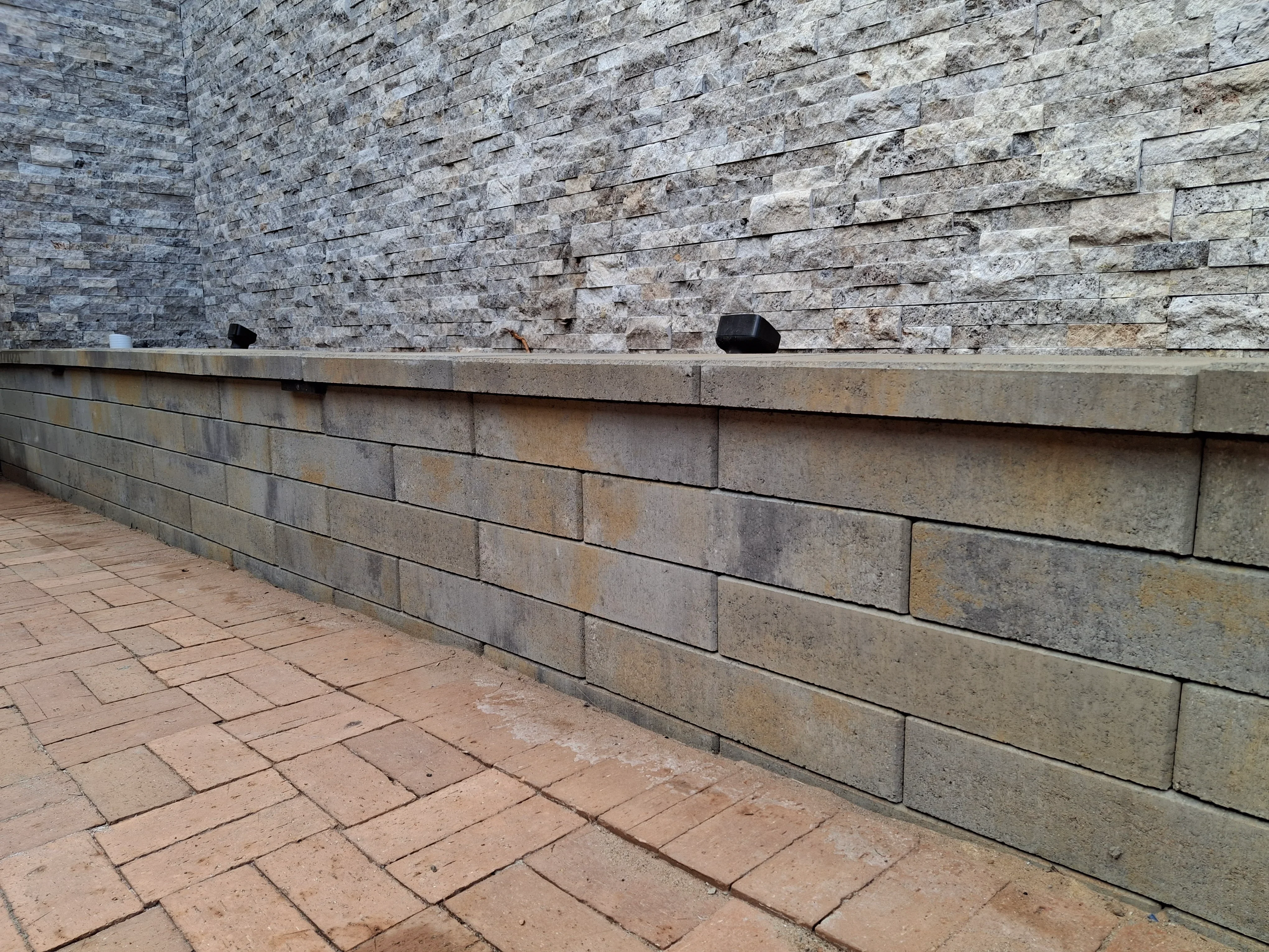 Tiered stone retaining wall with split-face veneer and concrete block base on brick paver patio