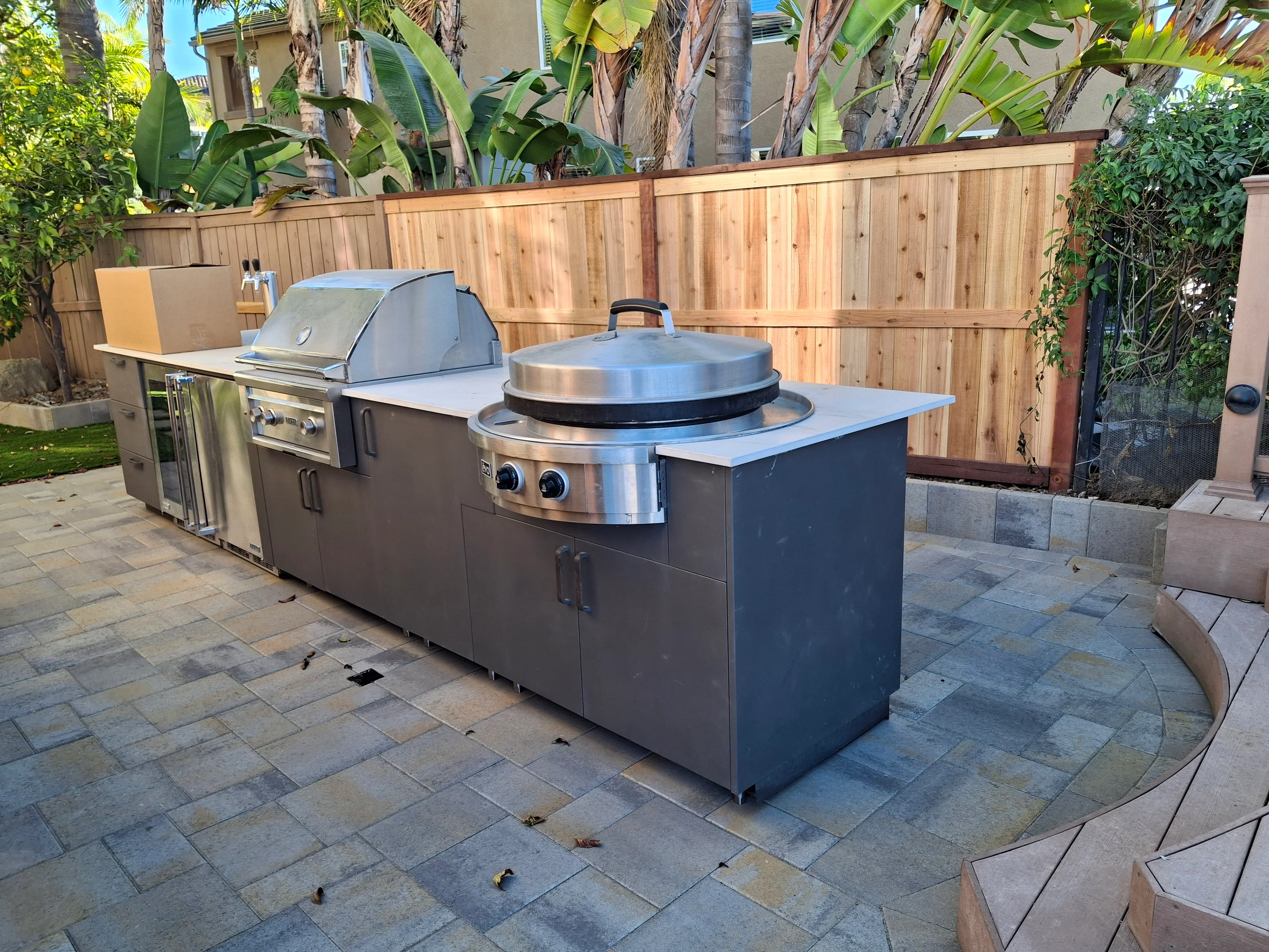 Stainless steel outdoor kitchen with grill, cooker, and refrigerator on multi-toned paver patio