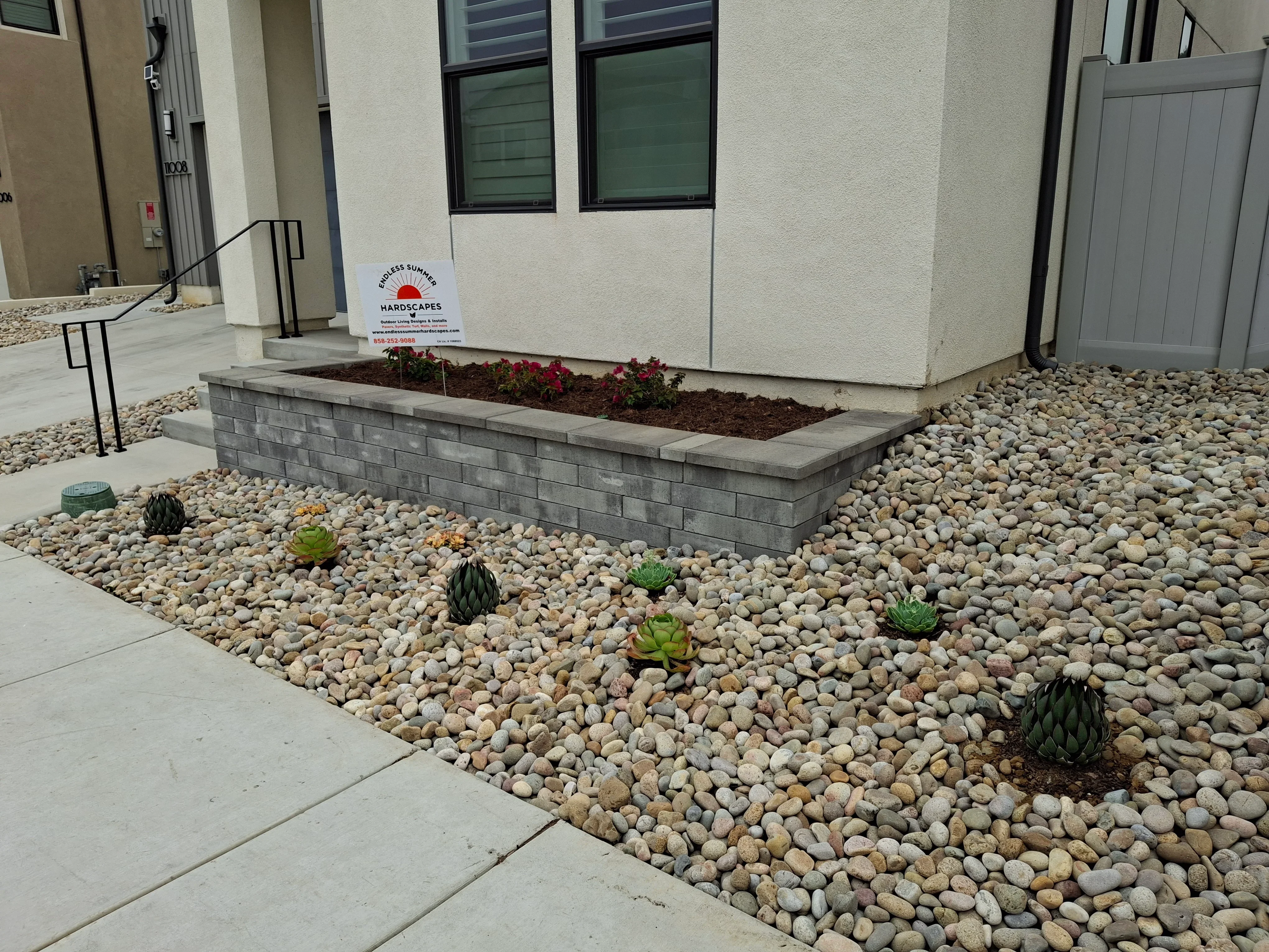 Raised concrete planter bed with river rock, gravel, and succulent plantings in front of building