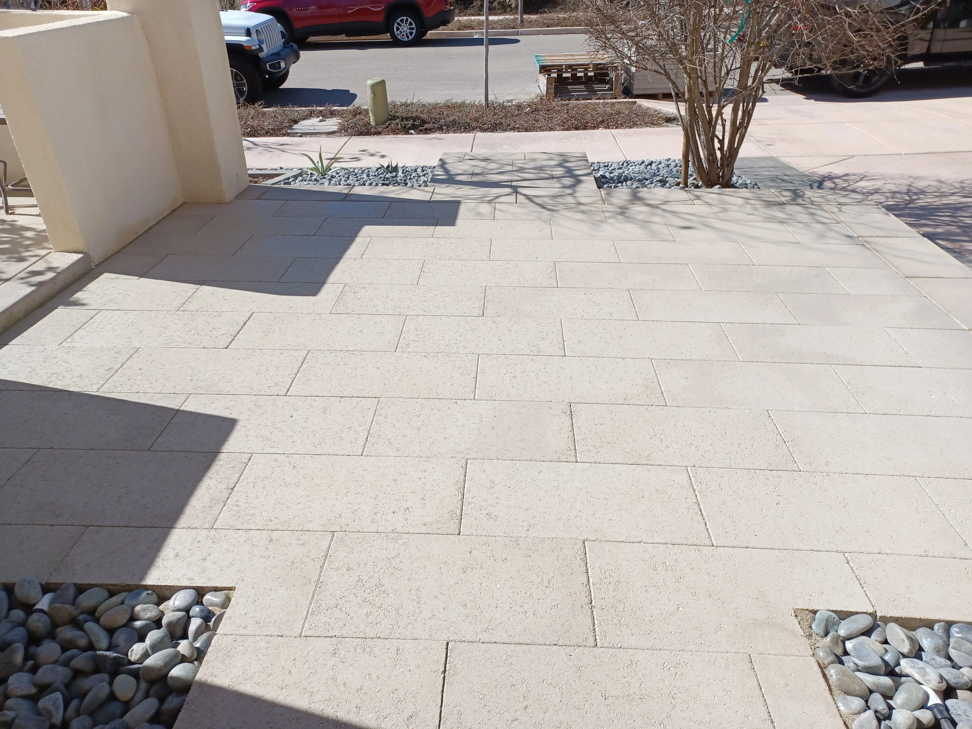 Light concrete pavers in running bond pattern with river rock borders and landscape beds