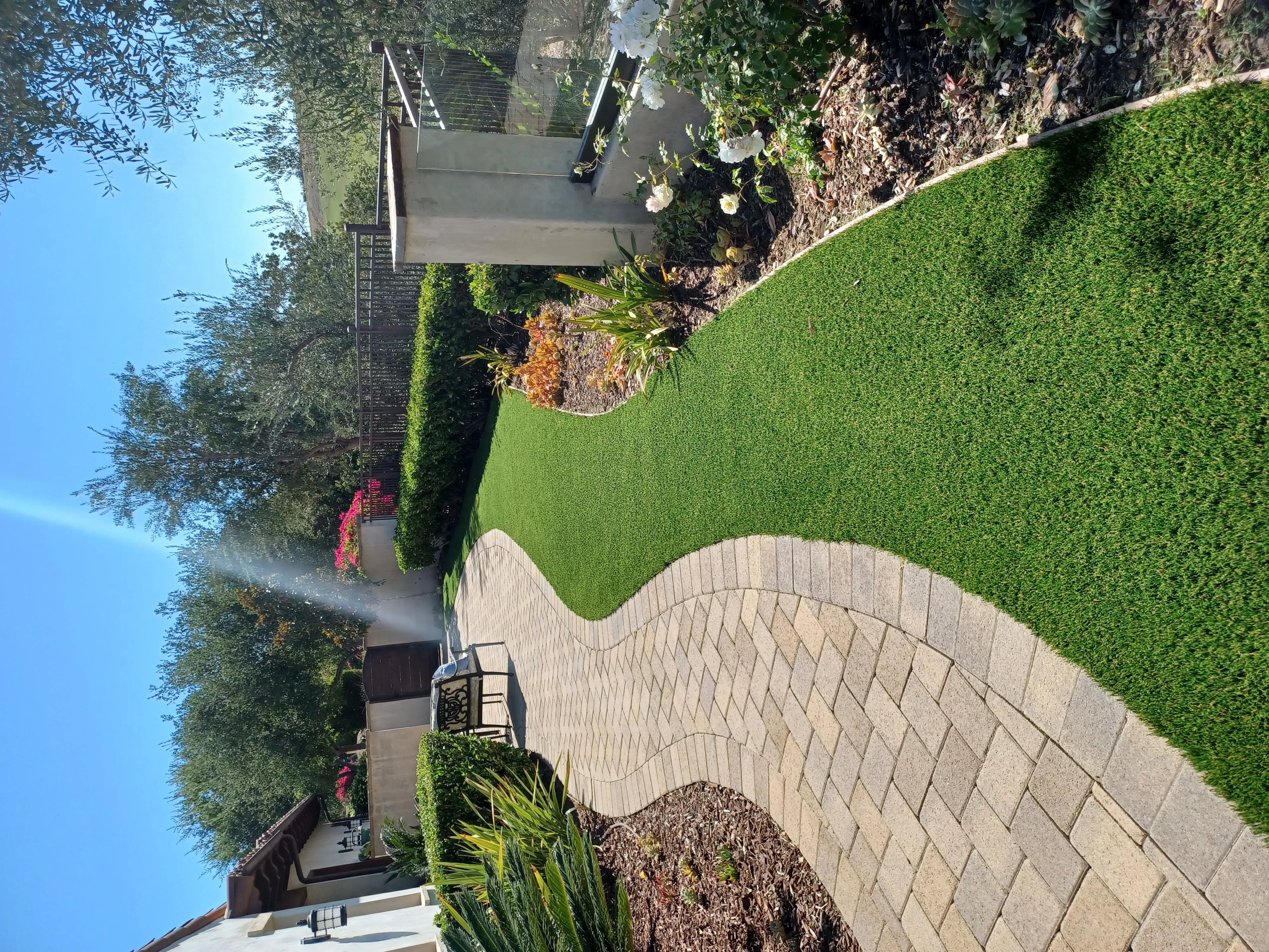 Curved paver patio with herringbone pattern, green lawn, and planted borders