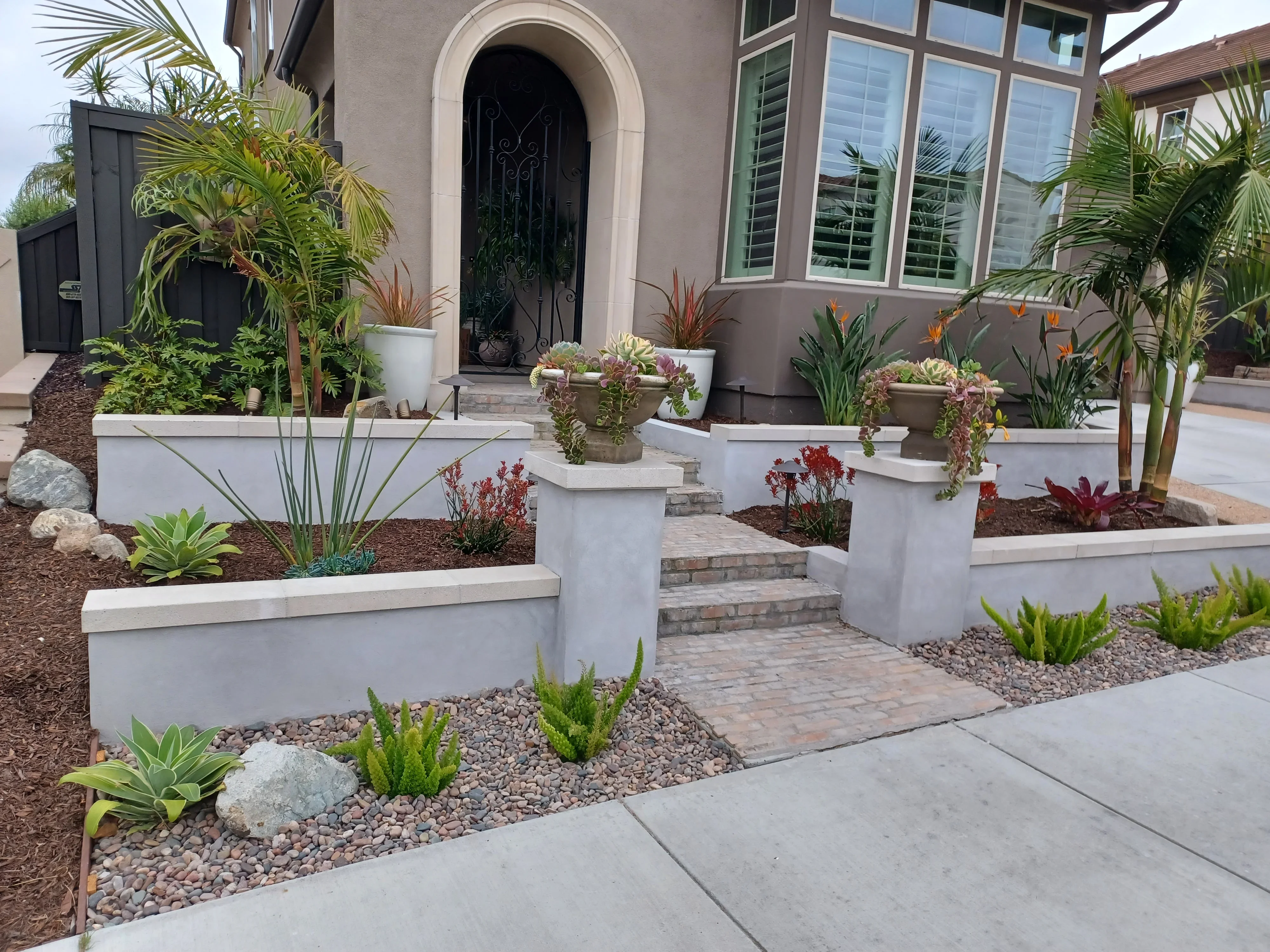 White raised planter beds, paver walkway, river rock mulch, and tropical plantings at residential entry