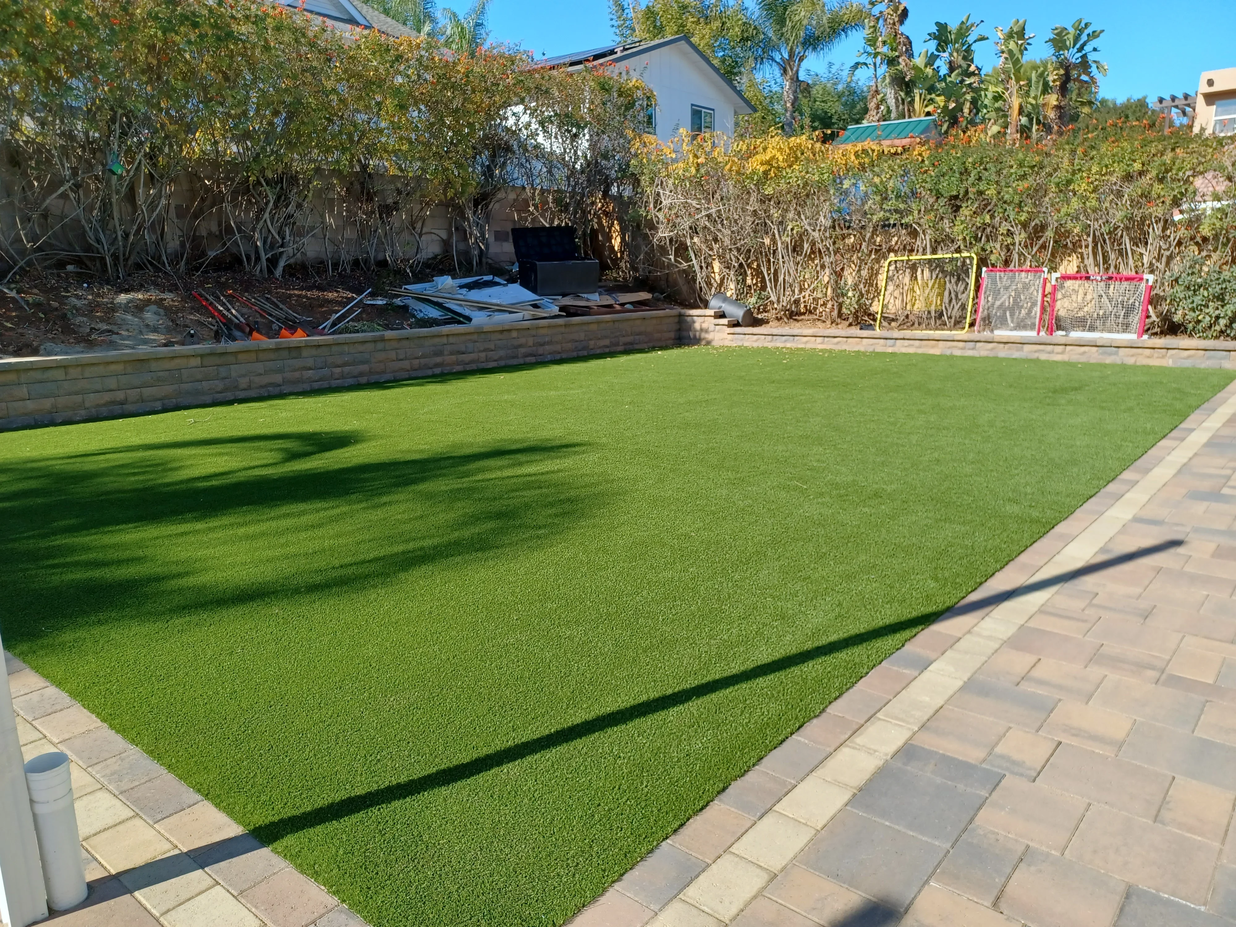 Synthetic turf lawn with paver border and stone retaining wall in residential backyard