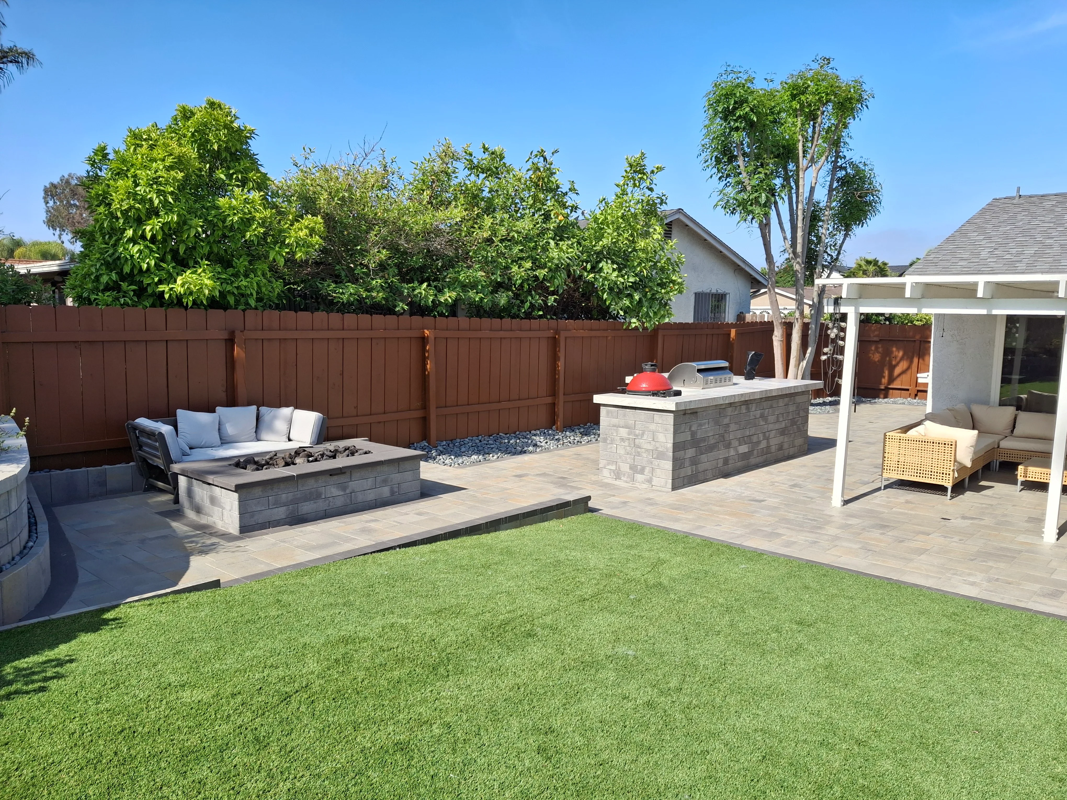 Paver patio with concrete block fire pit, outdoor kitchen island, and pergola in residential backyard