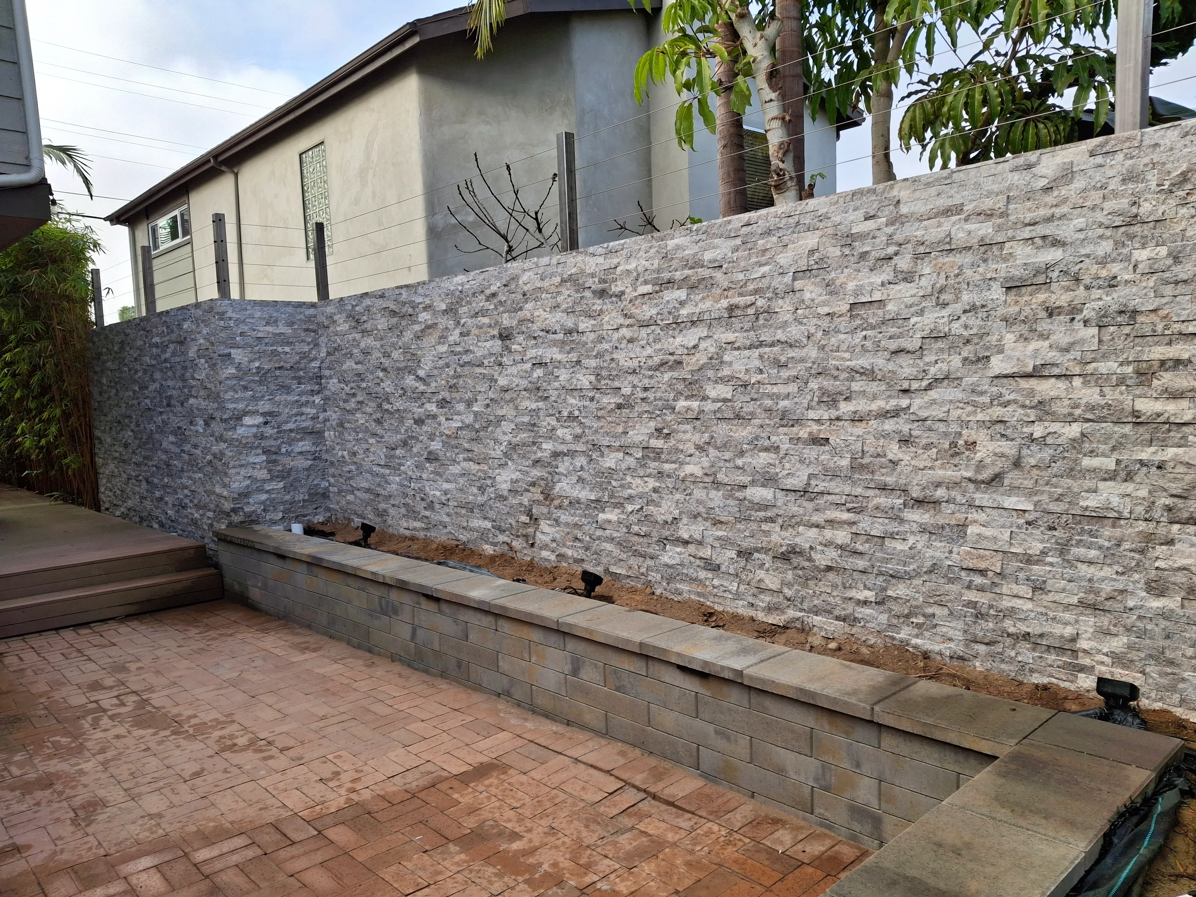 Stacked stone retaining wall with split-face ashlar blocks and concrete base on brick patio
