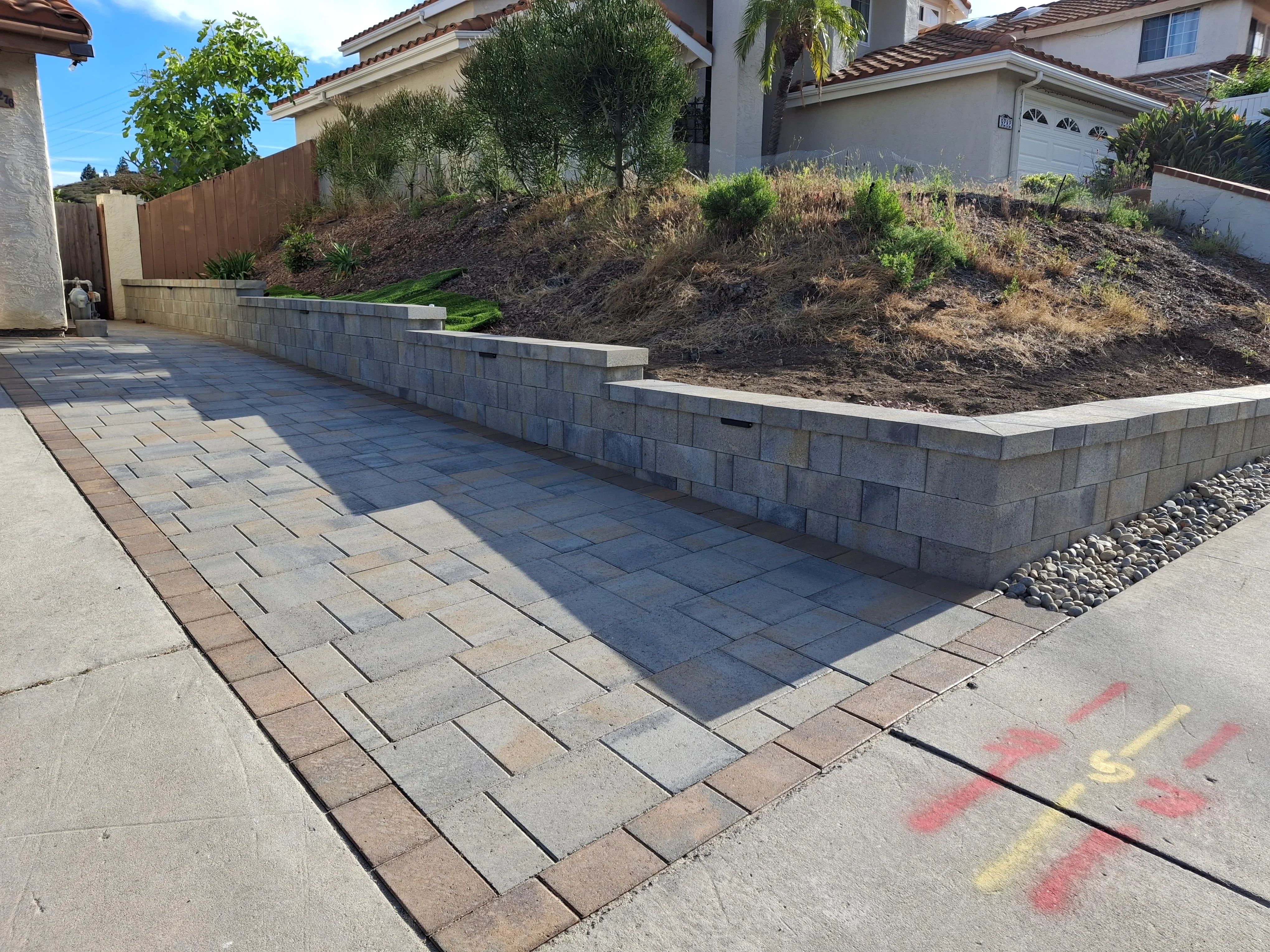 Permeable paver patio with running bond pattern and multi-tier concrete block retaining wall