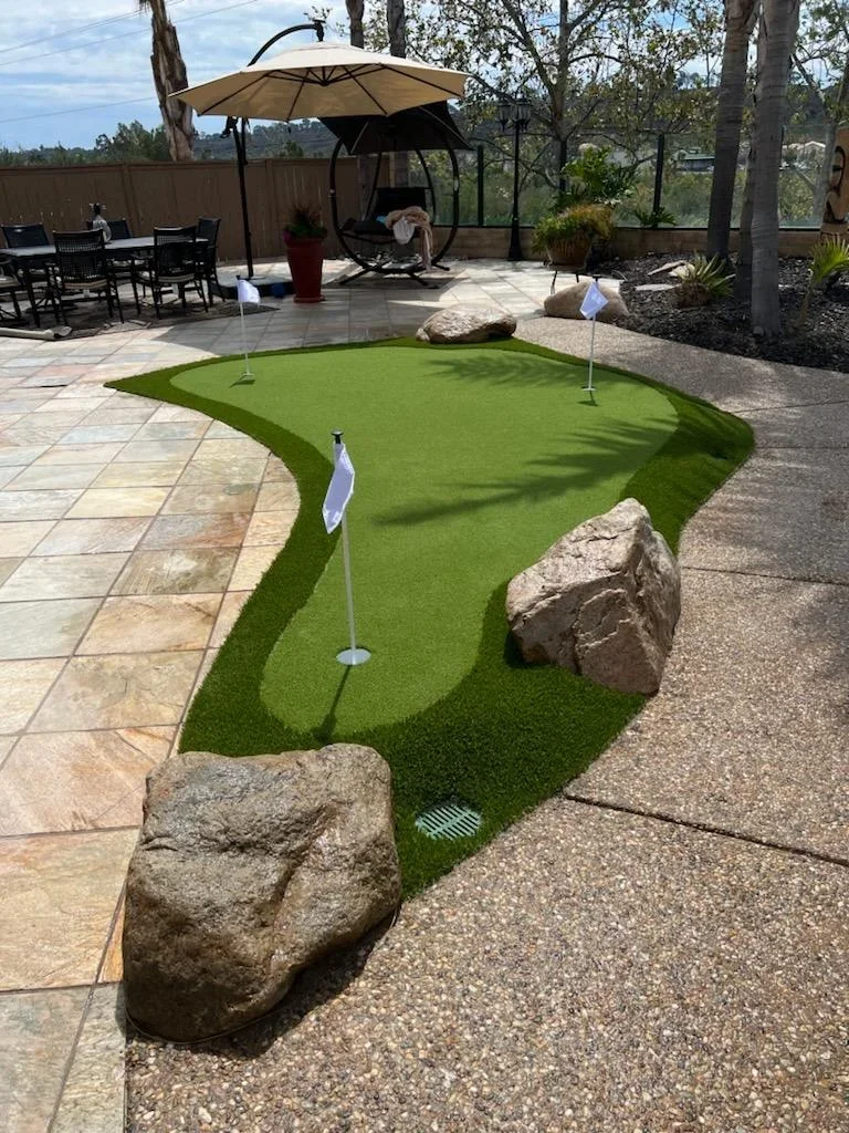 Synthetic putting green with flags and boulder borders on travertine paver patio