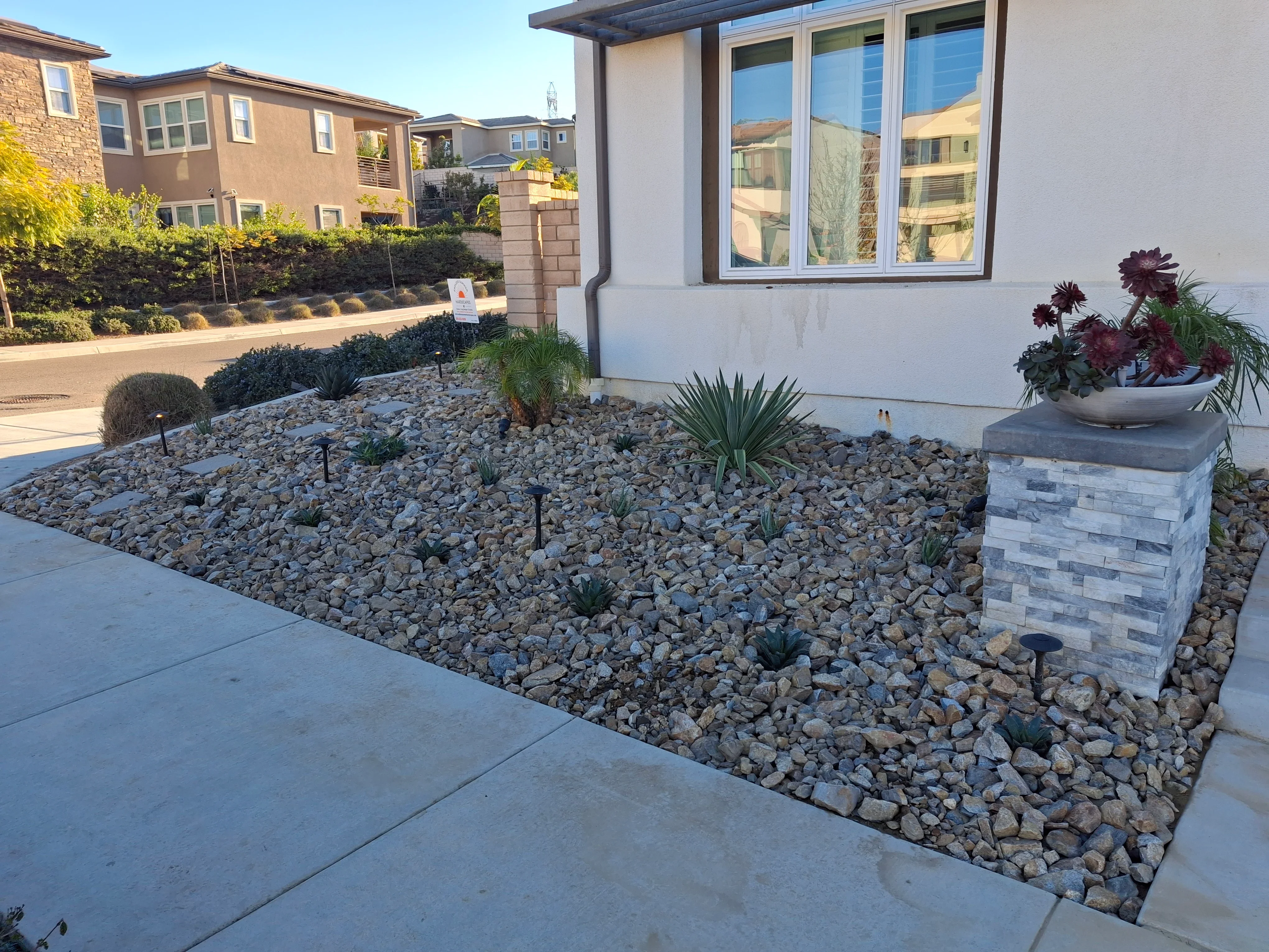 Decorative rock hardscape with stacked stone planter, concrete walkway, and drought-tolerant plants