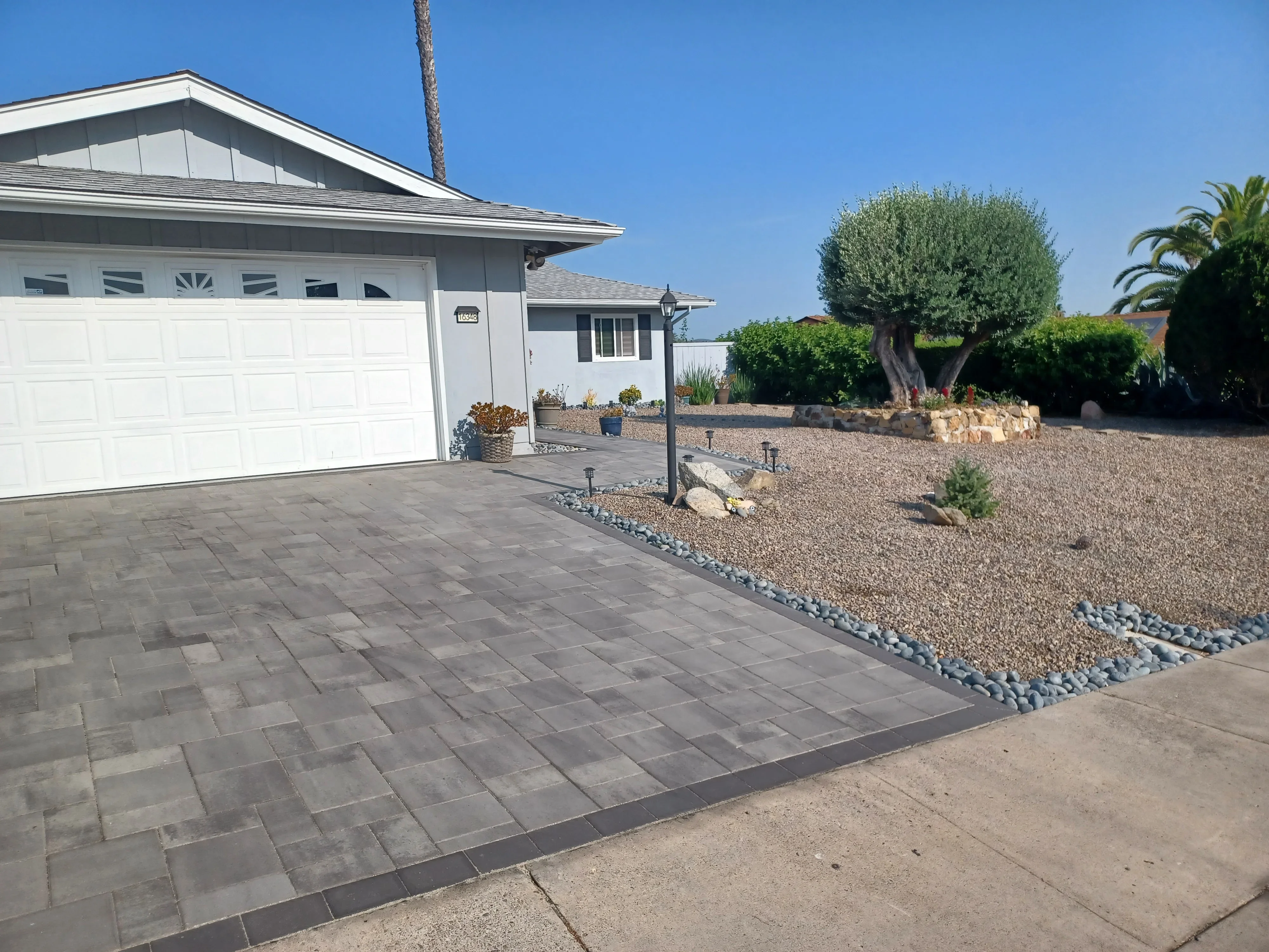 Gray permeable pavers driveway with dark border, gravel yard, and landscape lighting