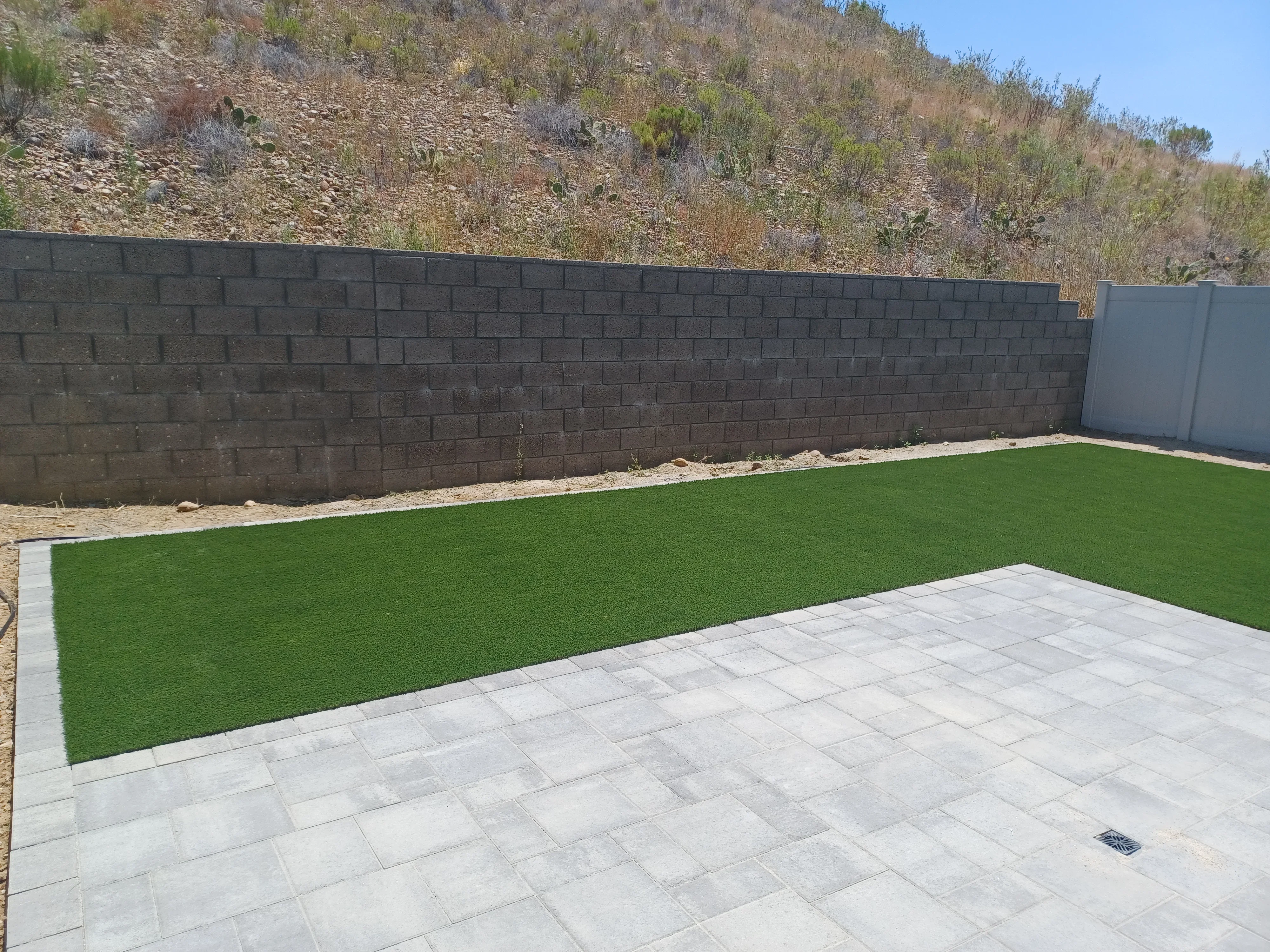 Concrete paver patio with synthetic turf and dark concrete block retaining wall