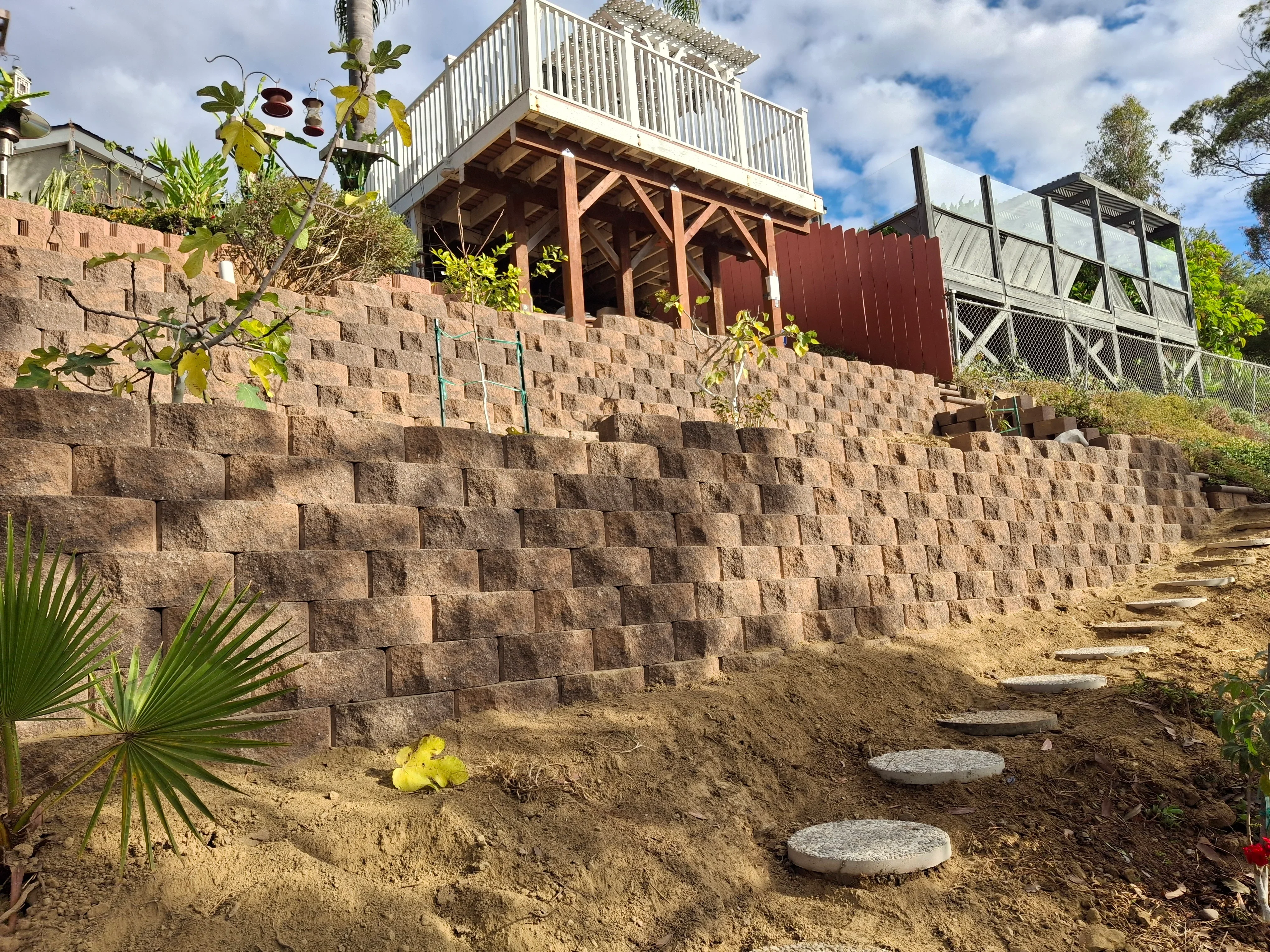 Stacked concrete block retaining wall with stepping stones and landscape plantings on sloped terrain