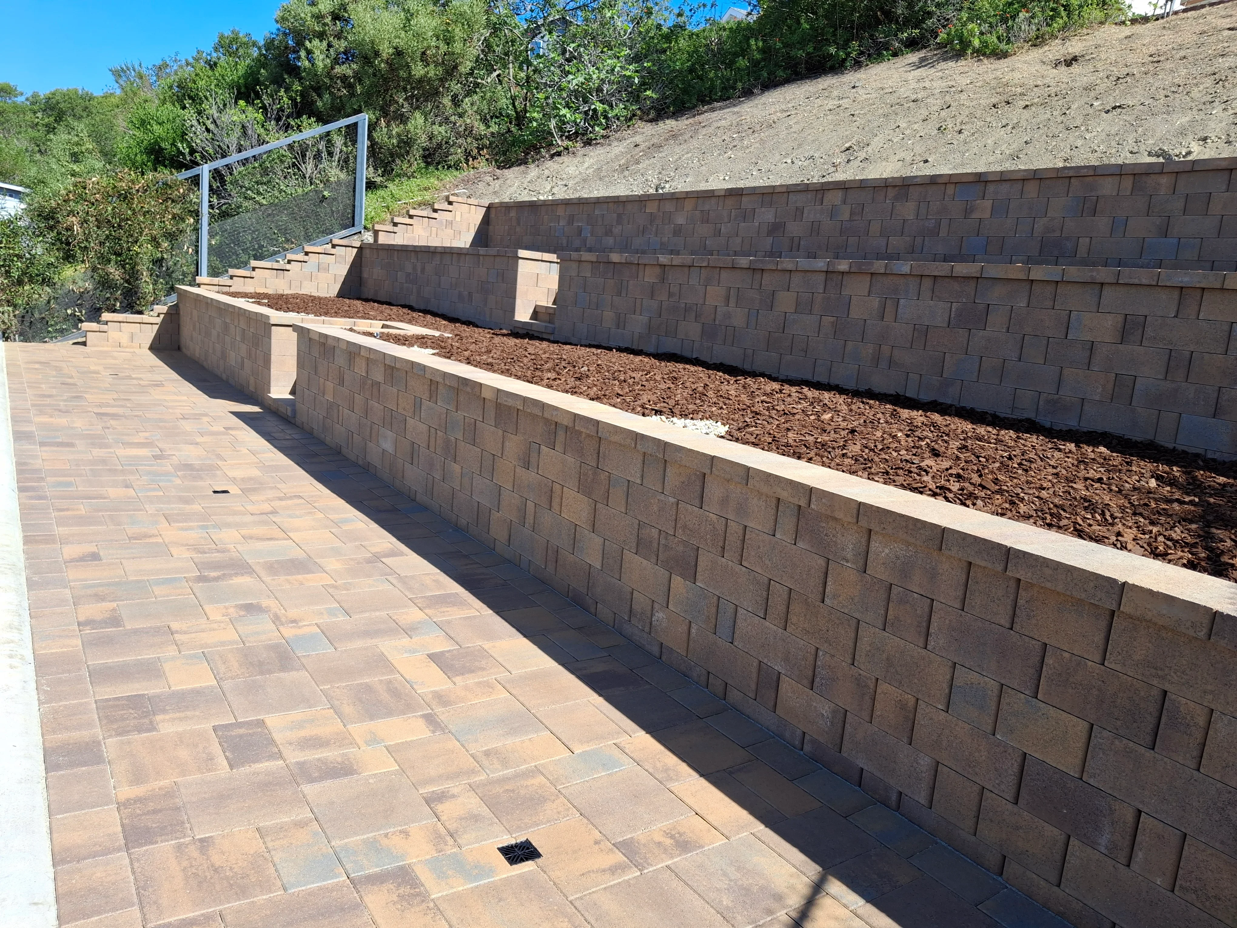 Tan concrete block retaining walls with mulch planters and paver patio with metal railing
