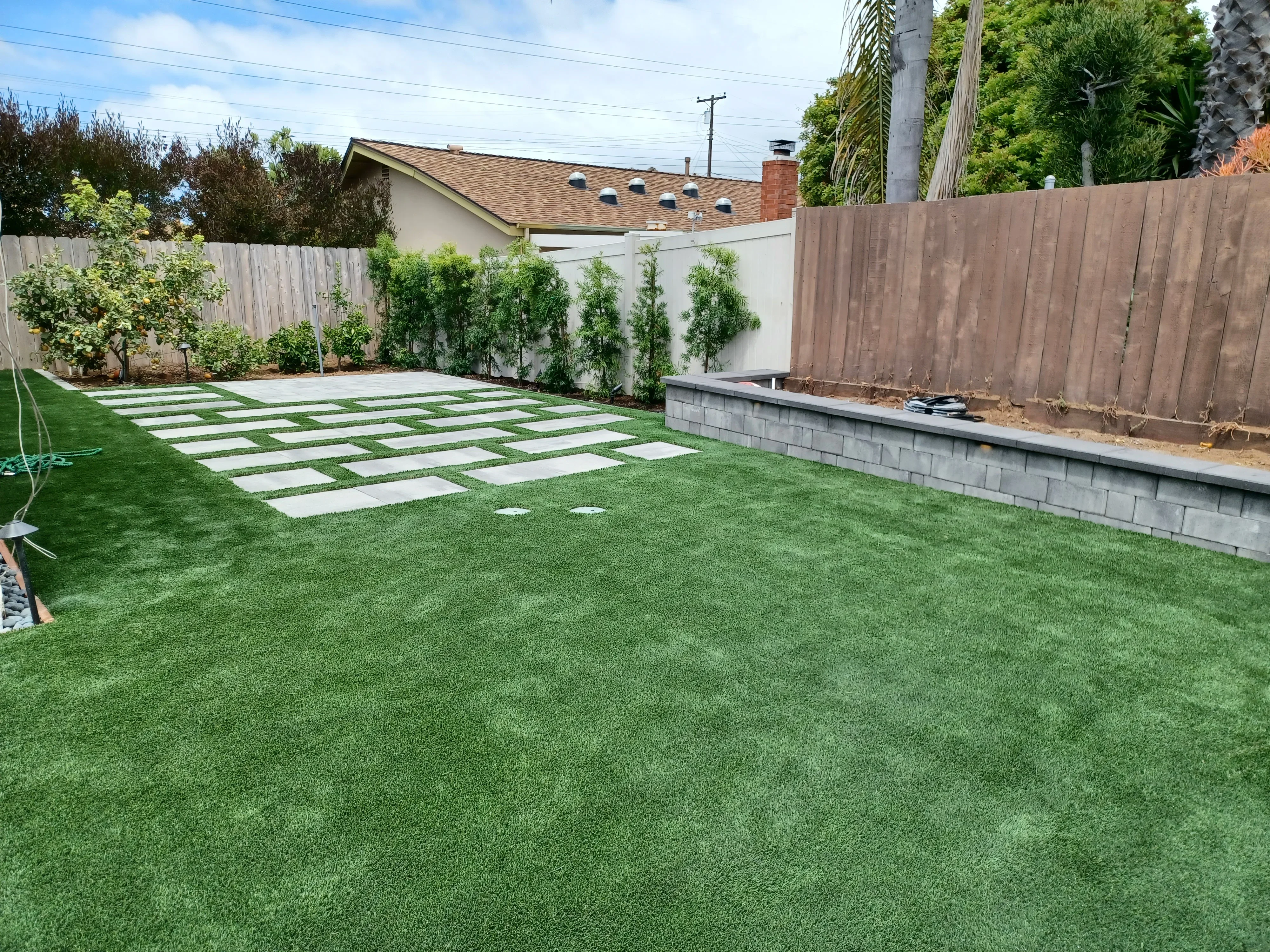 Concrete pavers with grass strips, retaining wall, and artificial turf in residential backyard