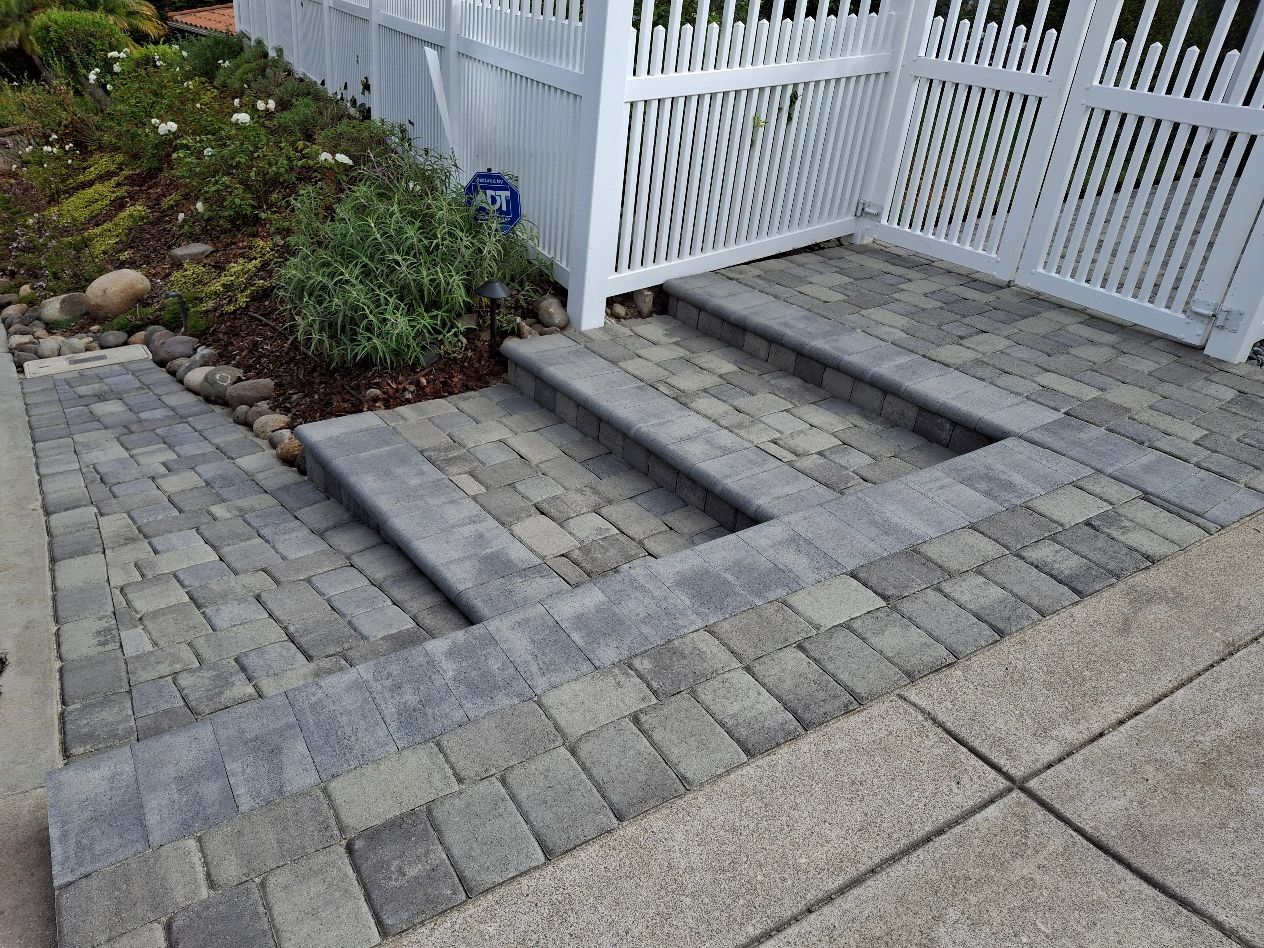 Gray permeable pavers with linear drainage channels, stone edging, and landscape bed integration