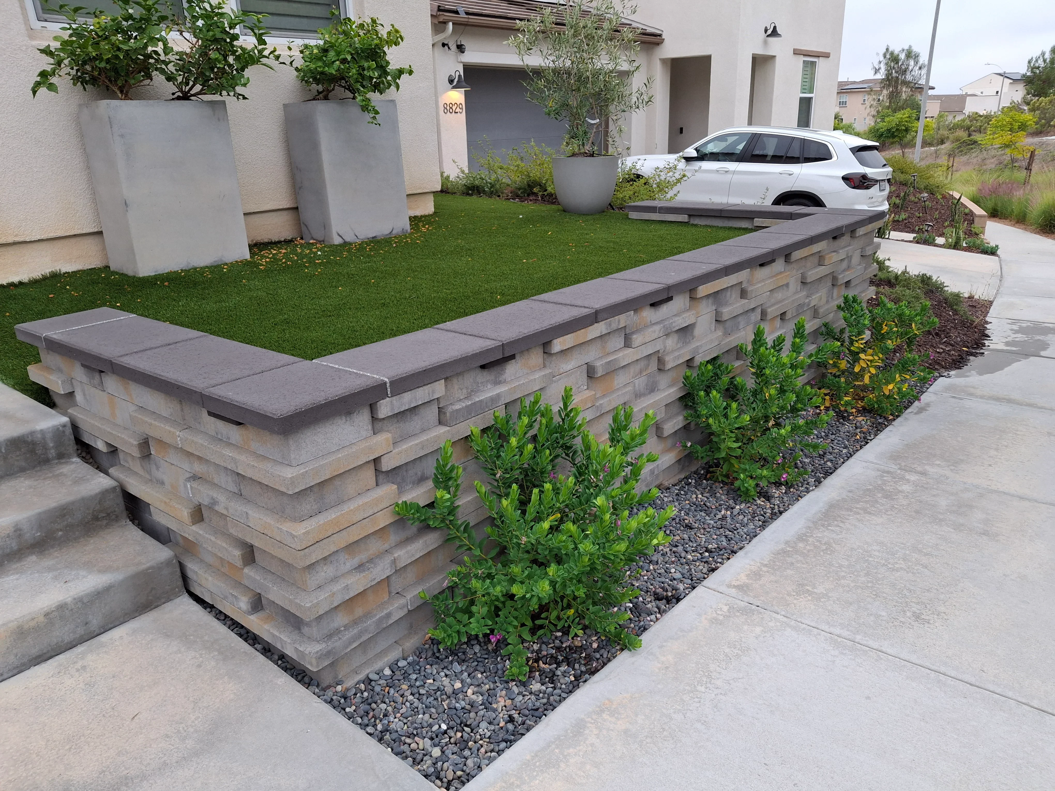 Stacked stone retaining wall with cap seating, gravel base, and shrub plantings