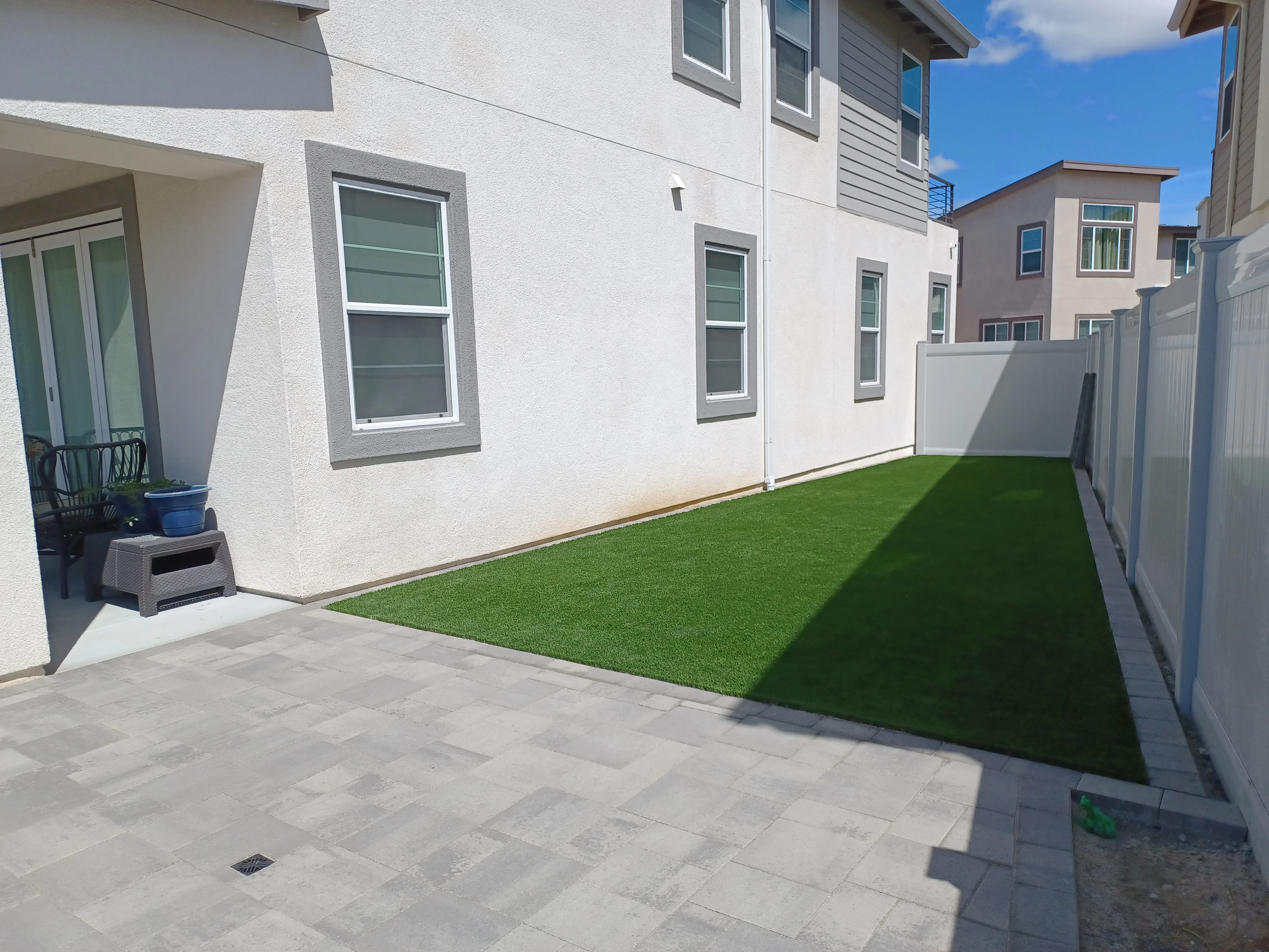 Light gray concrete paver patio with synthetic turf lawn and white vinyl fencing
