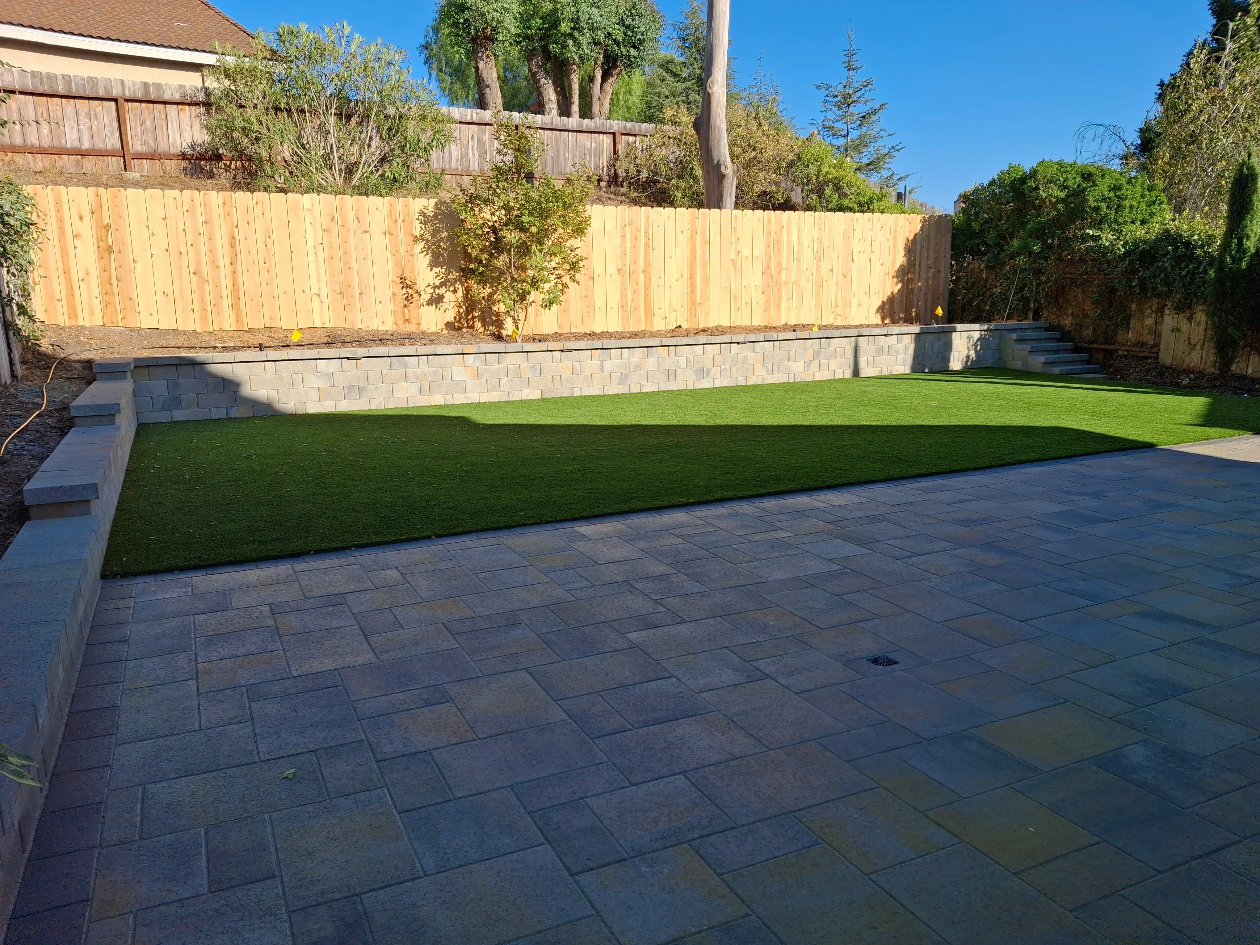 Charcoal paver patio with concrete block retaining wall and synthetic turf lawn