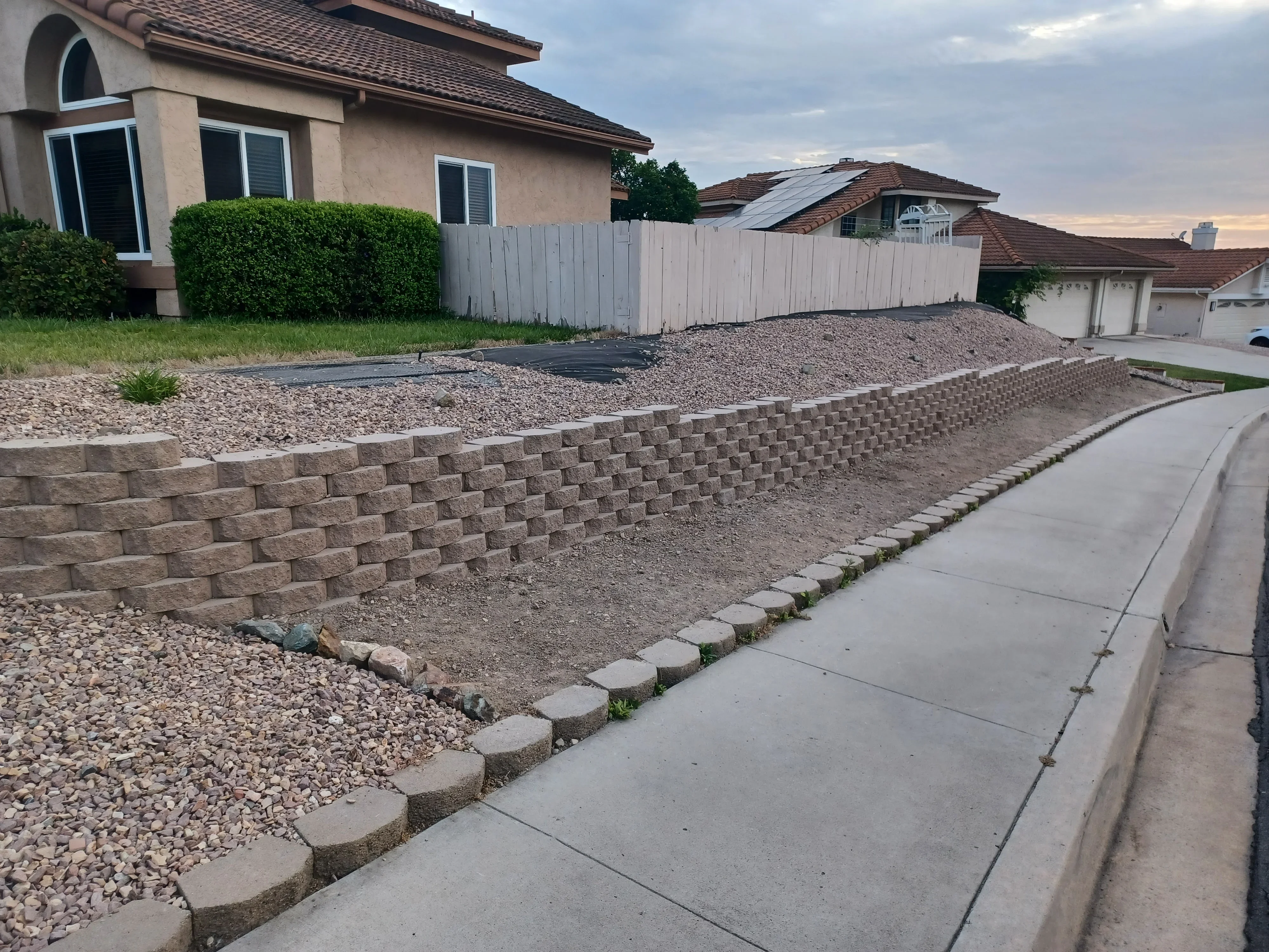 Concrete block retaining wall with gravel fill, concrete edging, and landscape fabric on residential property