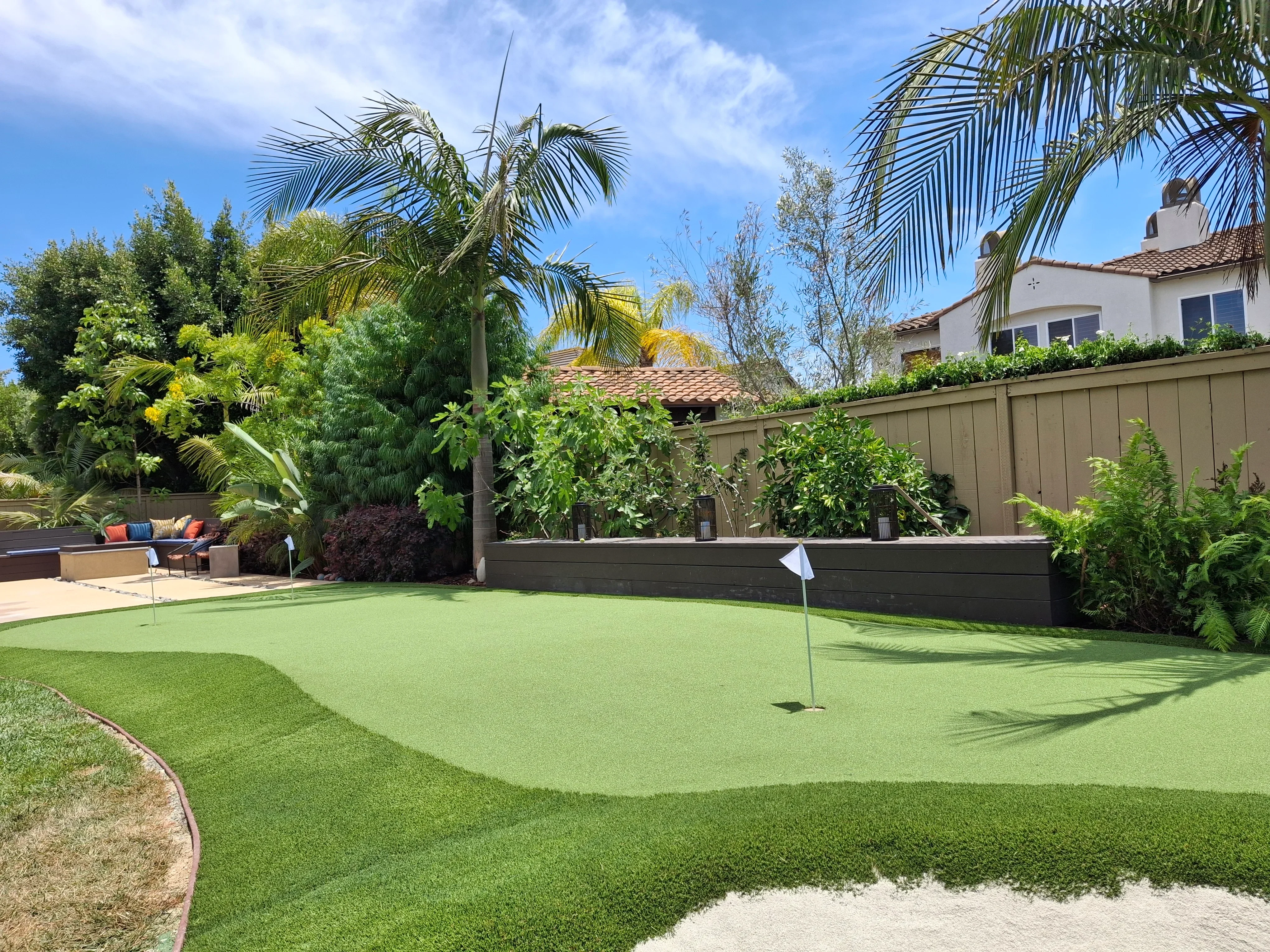 Synthetic putting green with sand bunker, composite fence, and mature landscape plantings