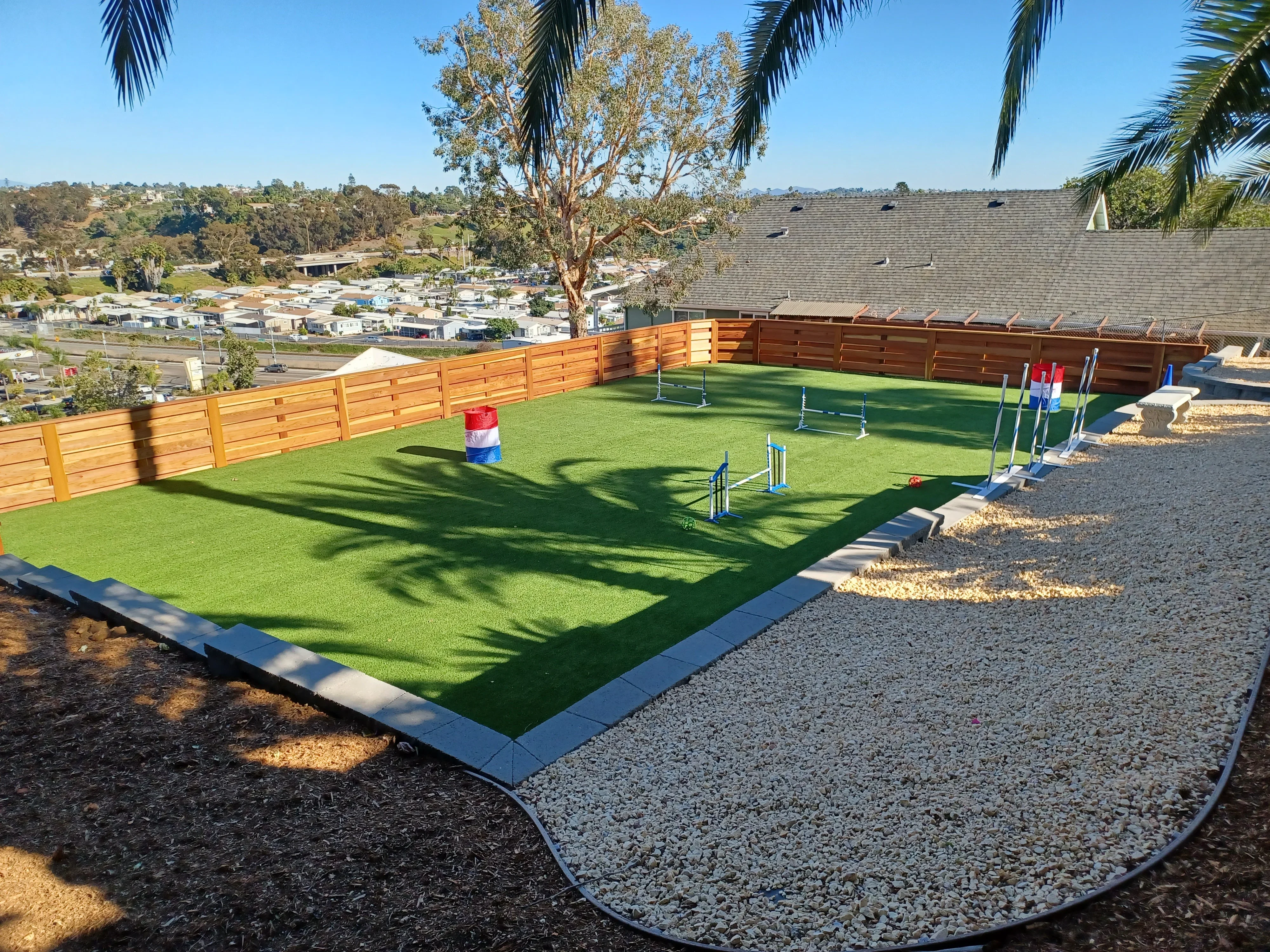 Synthetic turf equestrian arena with cedar fencing, gravel base, and concrete edging