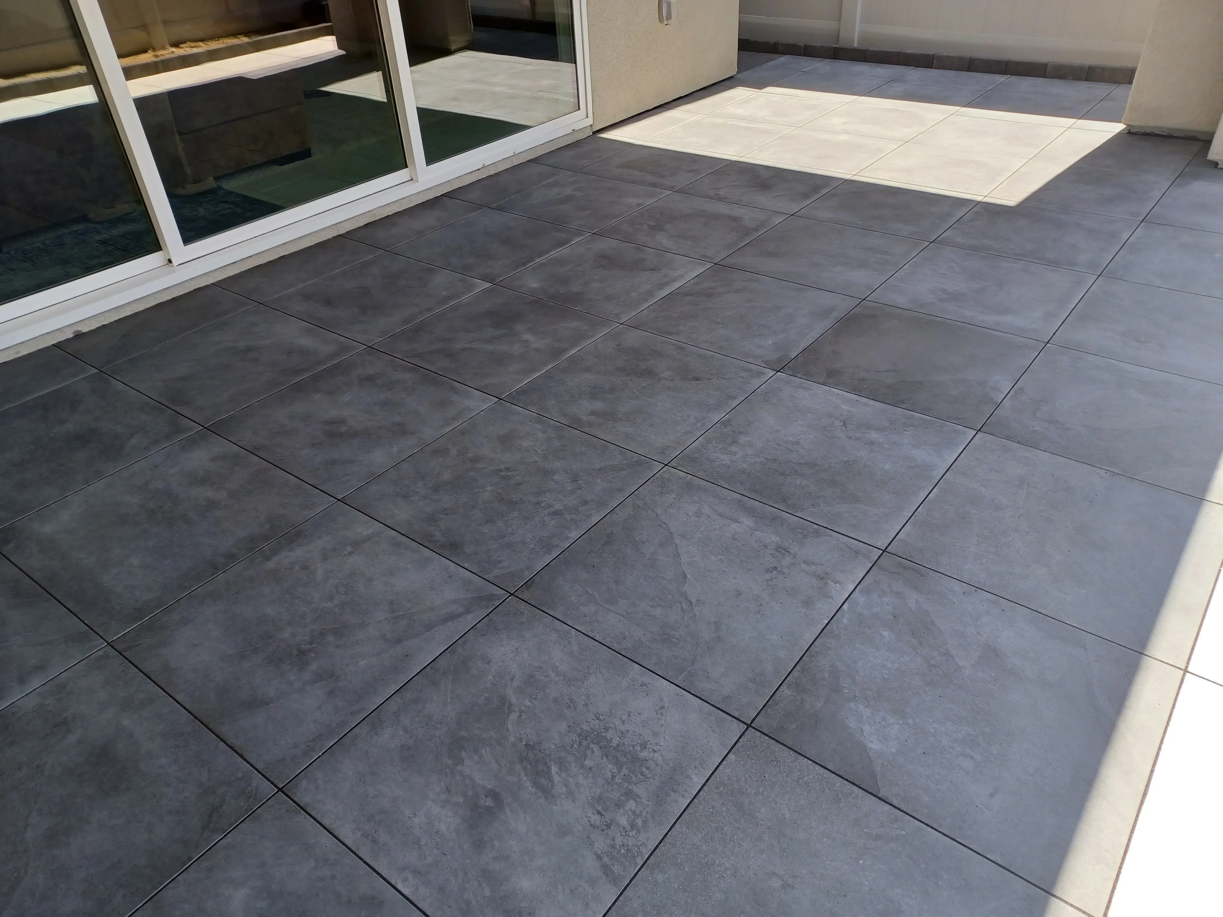 Dark gray porcelain tile patio with large-format tiles and grouted joints adjacent to glass doors