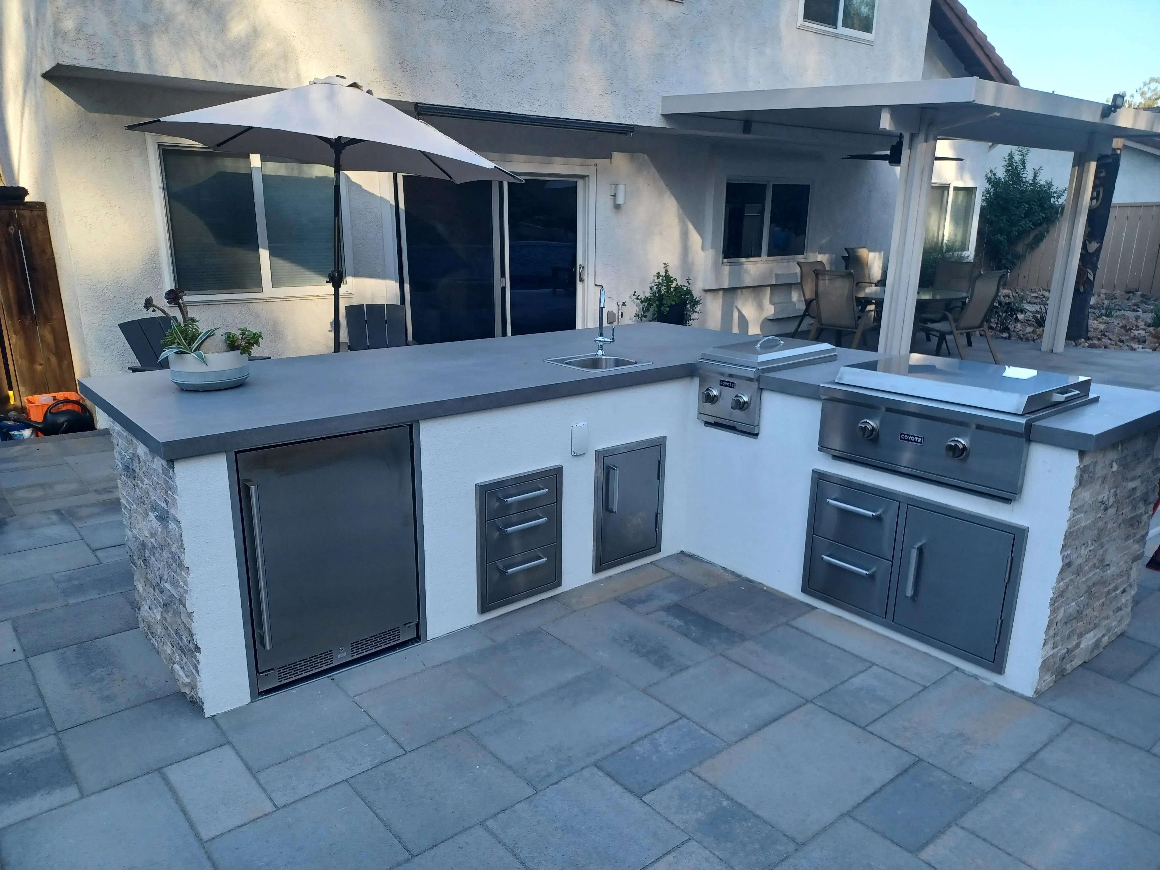 Outdoor kitchen island with stone veneer, stucco, metal cabinetry, and slate paver patio