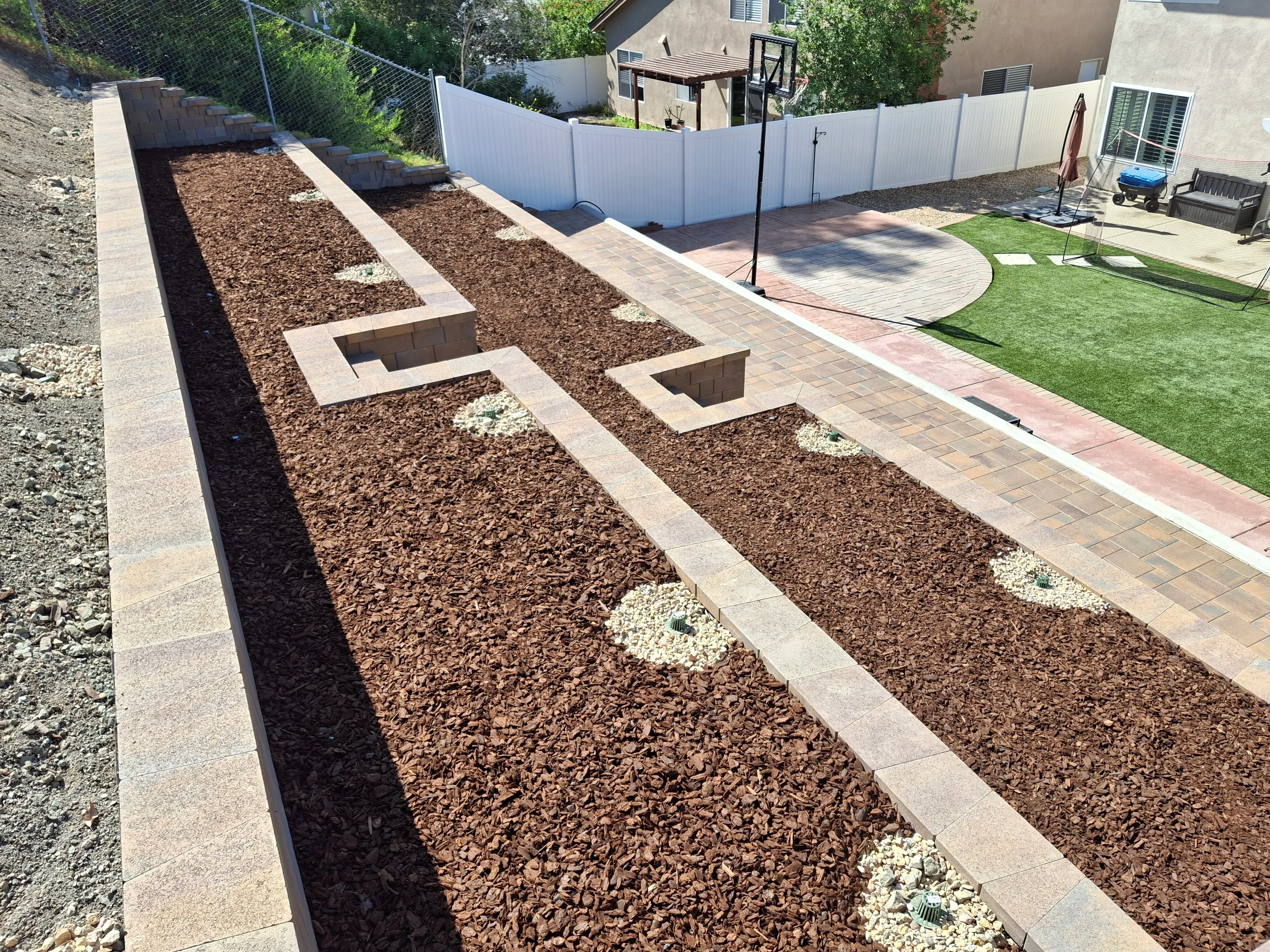 Concrete block raised garden beds with mulch, white rock accents, and clay brick paver patio installation