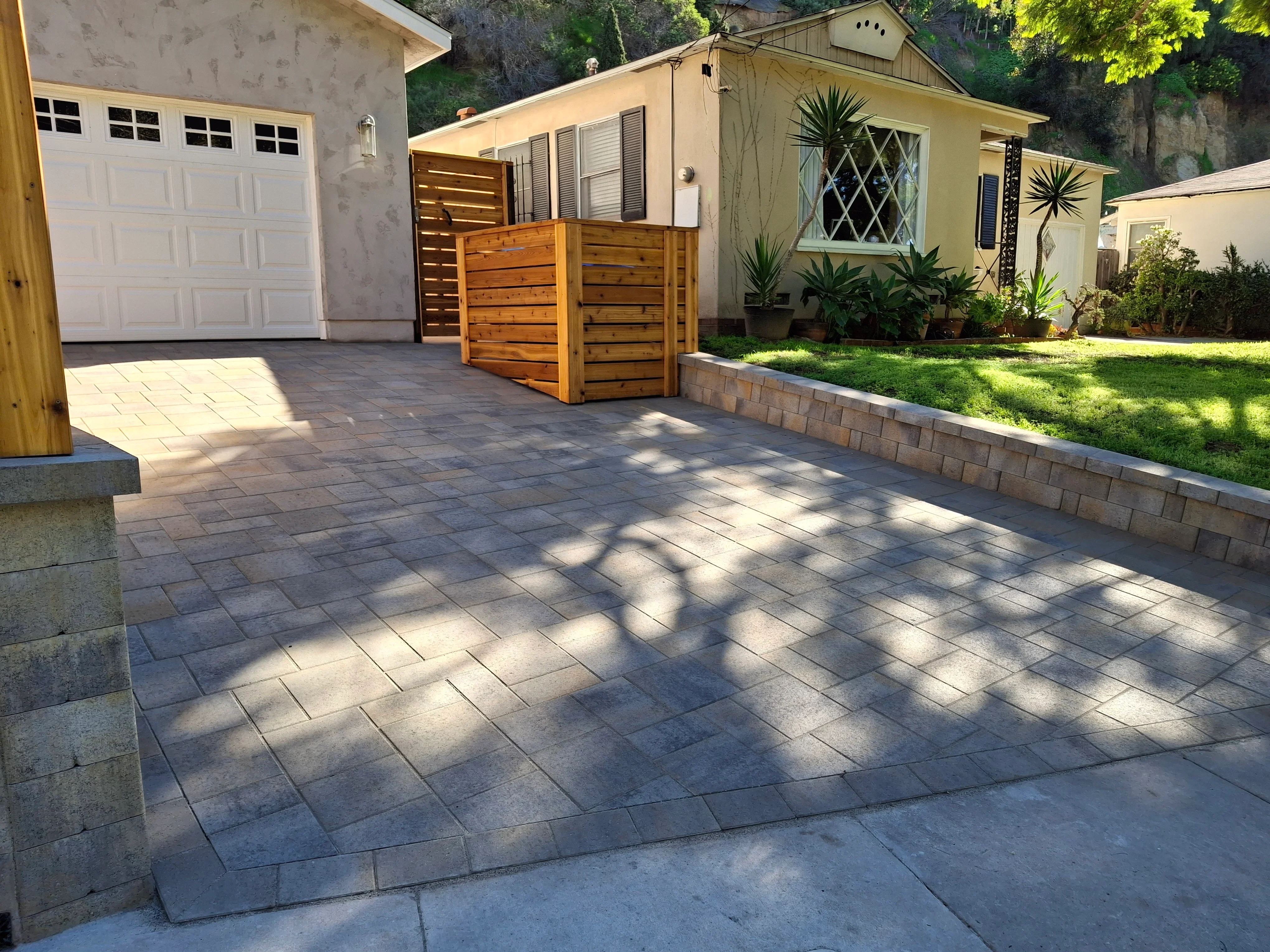 Gray concrete permeable pavers in running bond pattern with stone retaining wall and wooden privacy screen