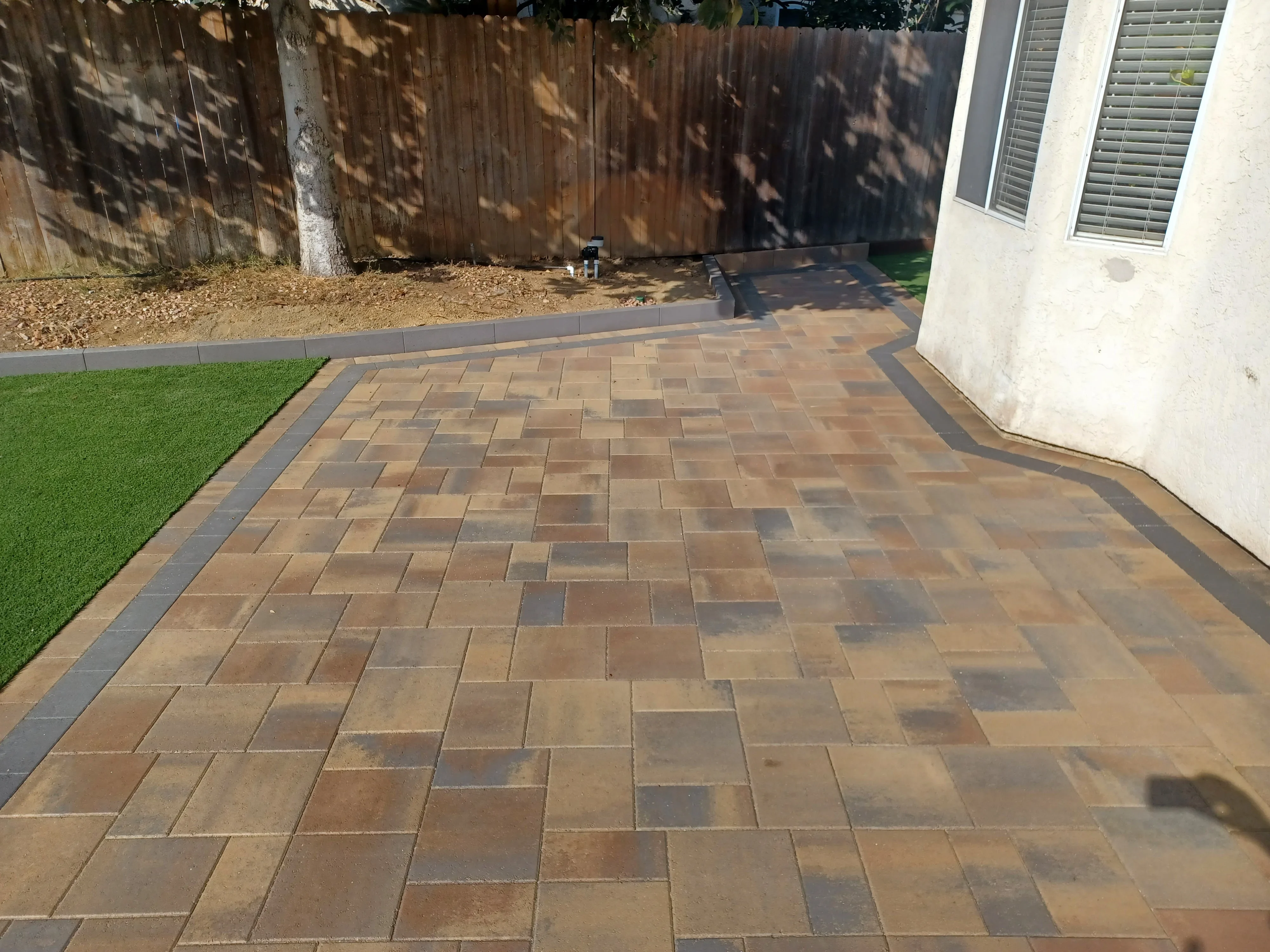 Warm-toned permeable pavers in mixed-size pattern with charcoal border, curved layout against home foundation