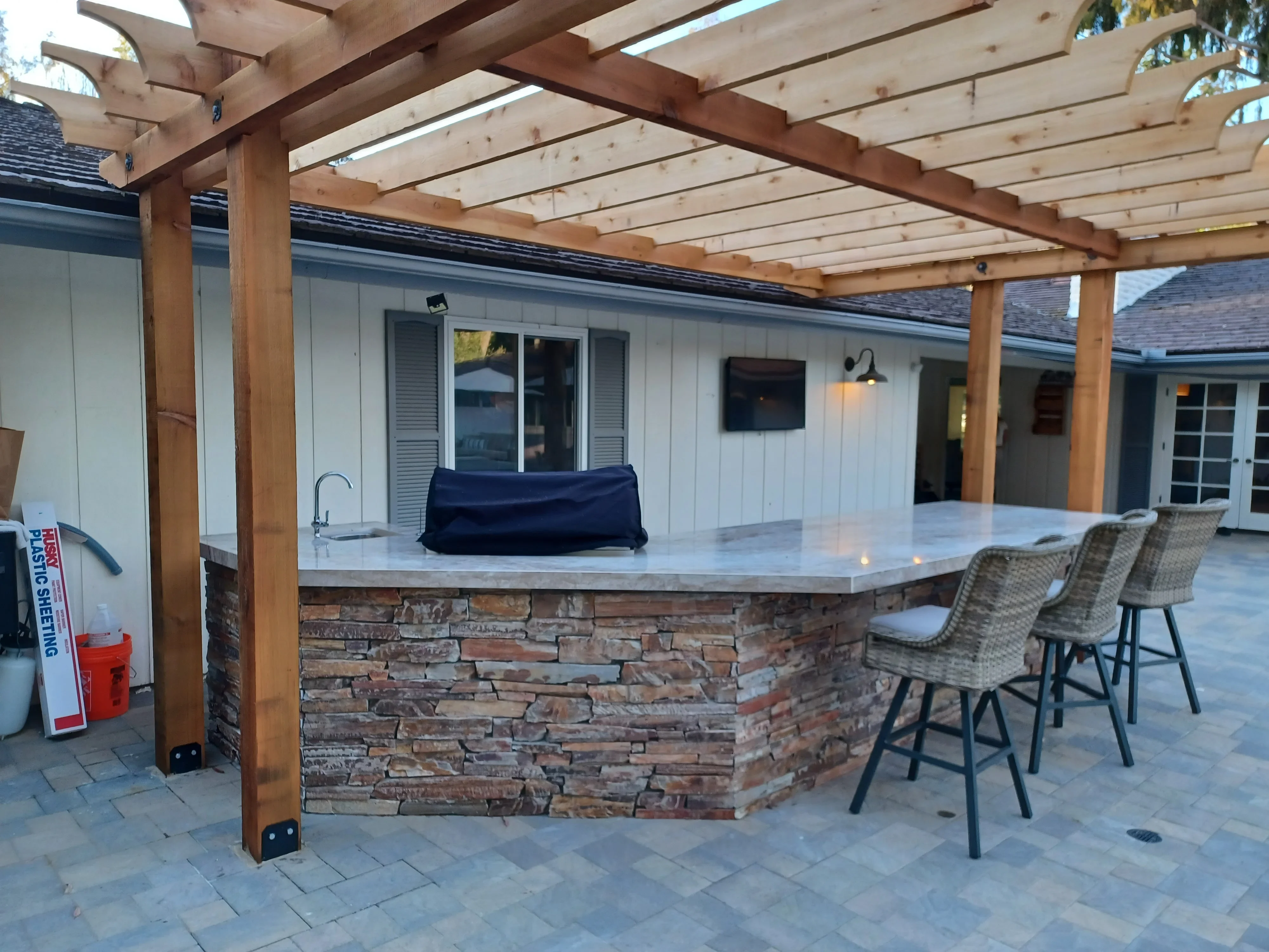 Stone veneer bar with quartz top, wood pergola, and paver patio in outdoor kitchen setting