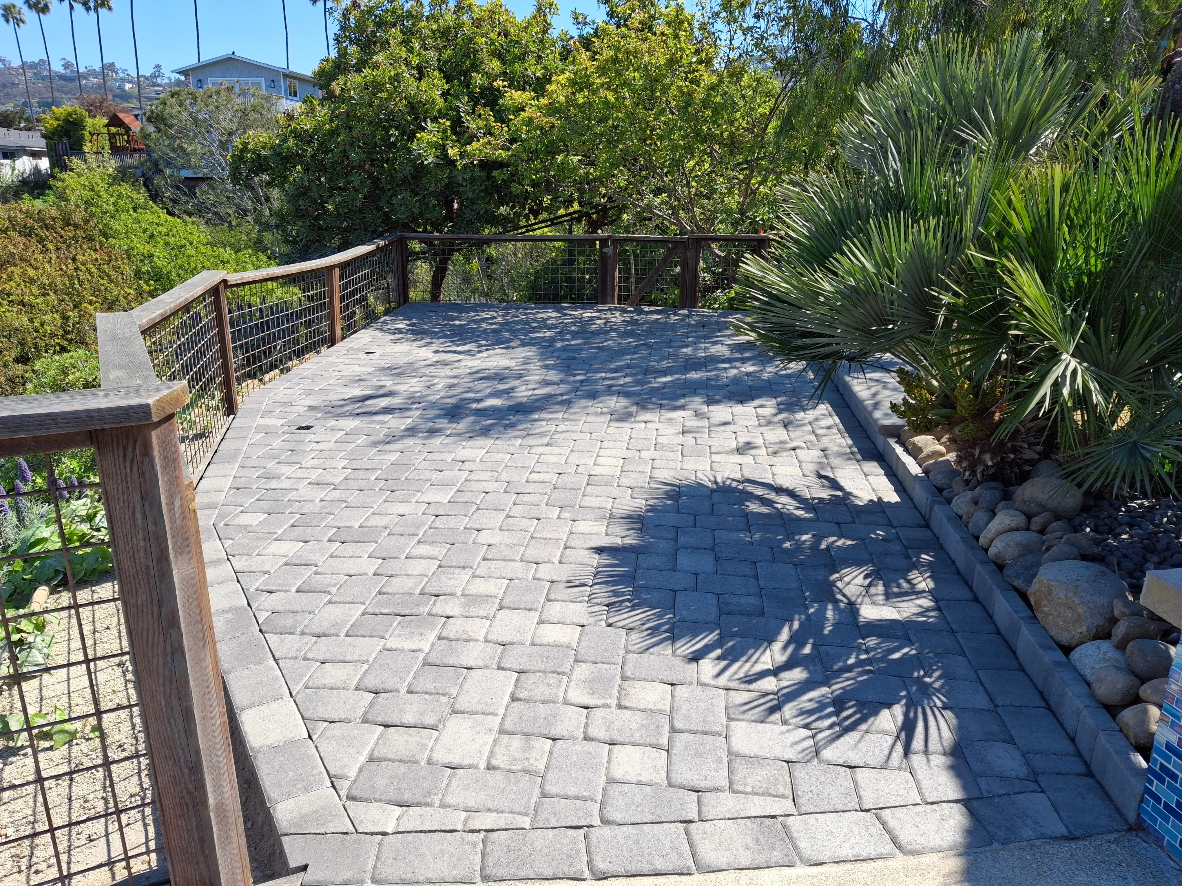 Gray paver deck with herringbone pattern, metal cable railing, and landscape edging with river rock