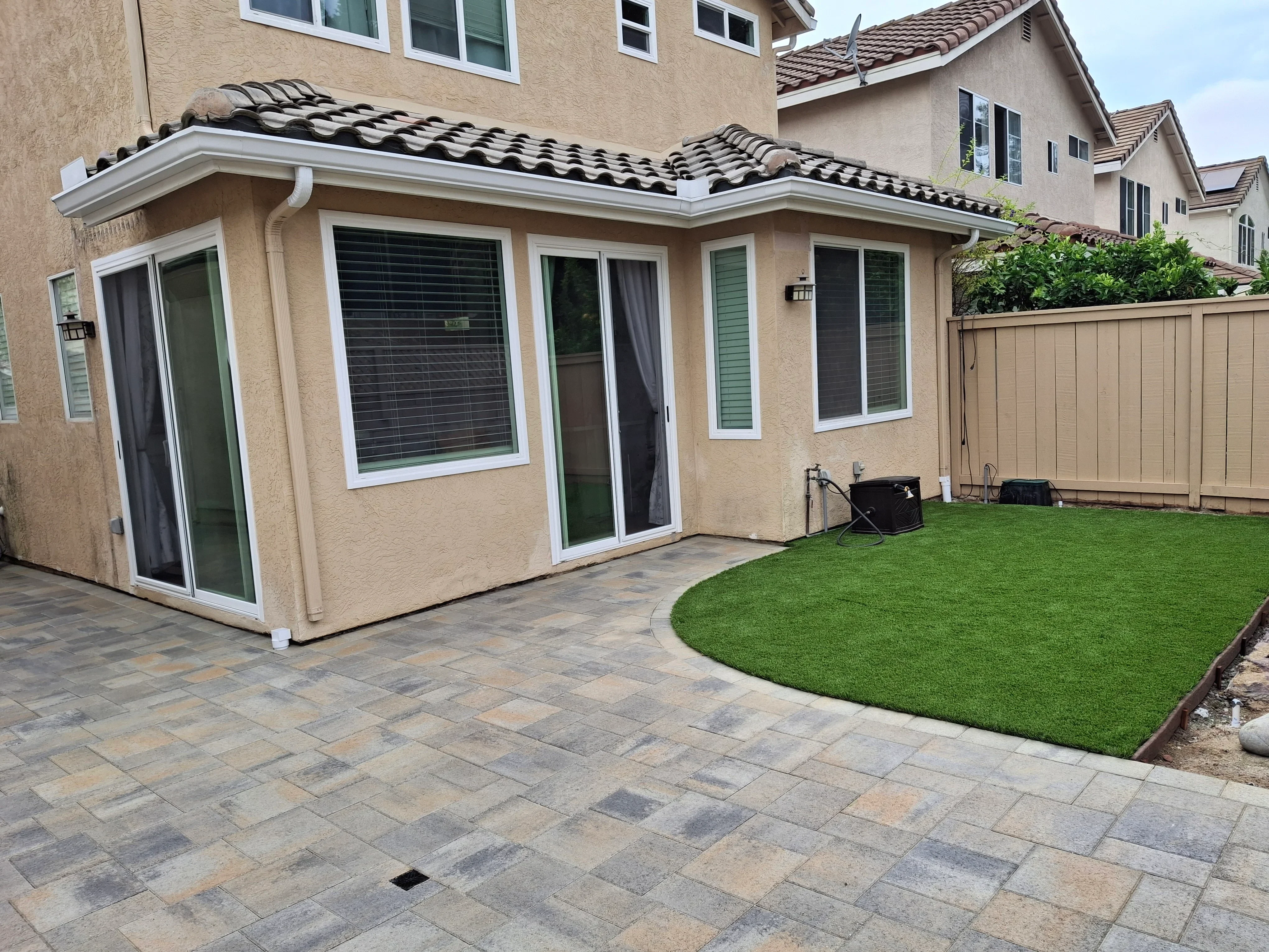 Permeable paver patio with synthetic turf, covered structure with Spanish tile roof, and composite fence