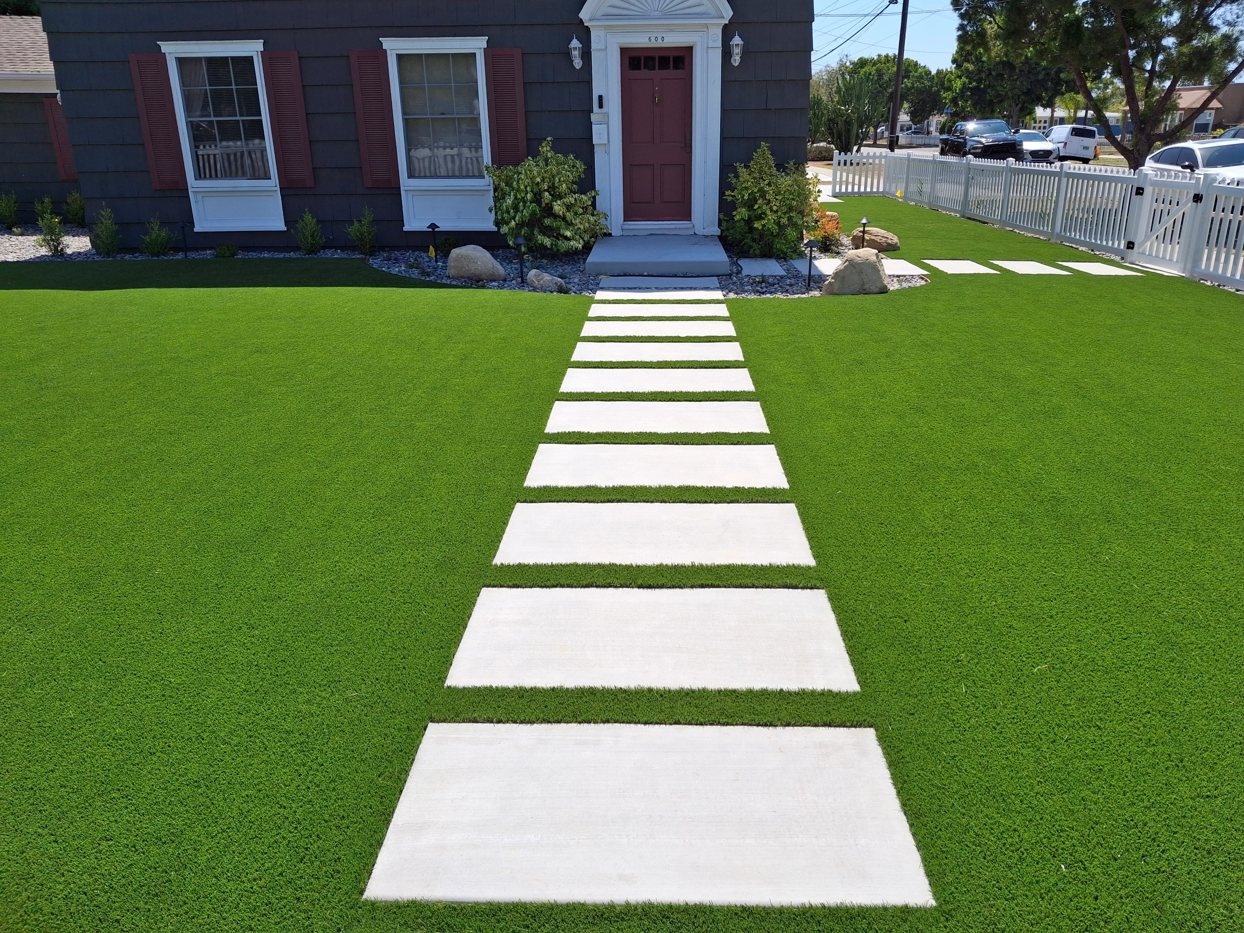 White concrete stepping stones through green synthetic turf leading to home entrance