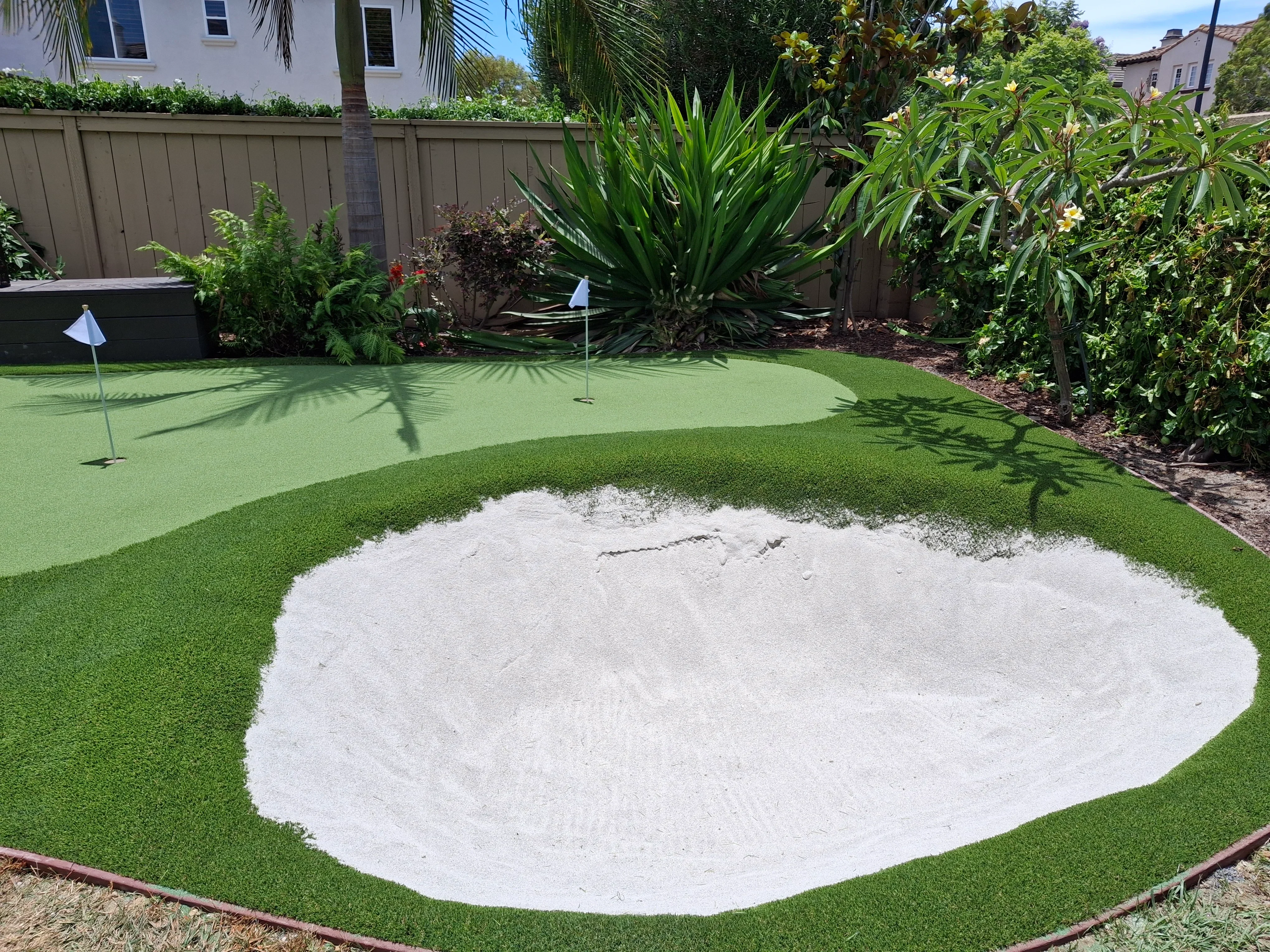 Synthetic putting green with sand bunker, flagsticks, and landscape borders in residential backyard