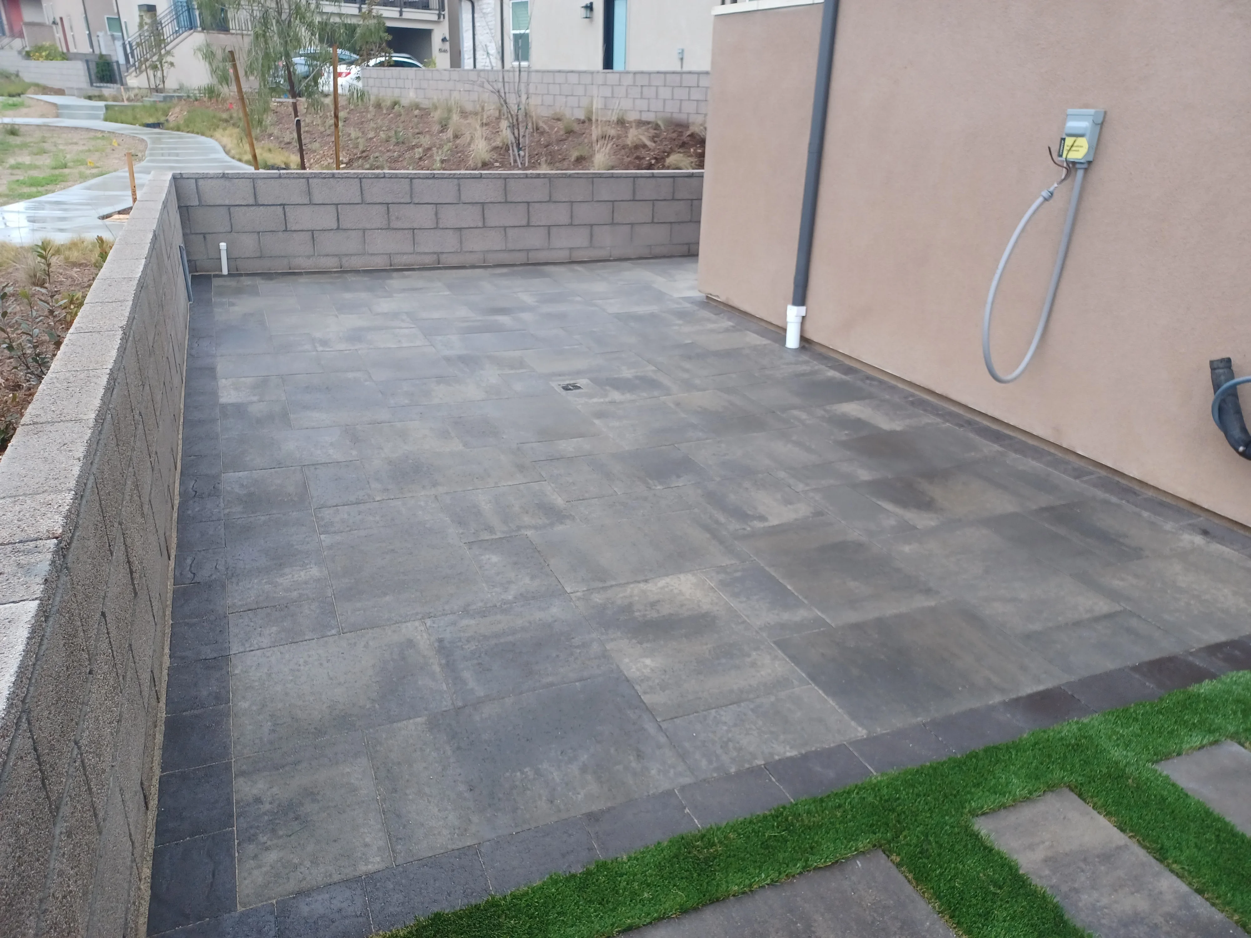 Dark gray porcelain paver patio with running bond pattern and concrete block retaining wall