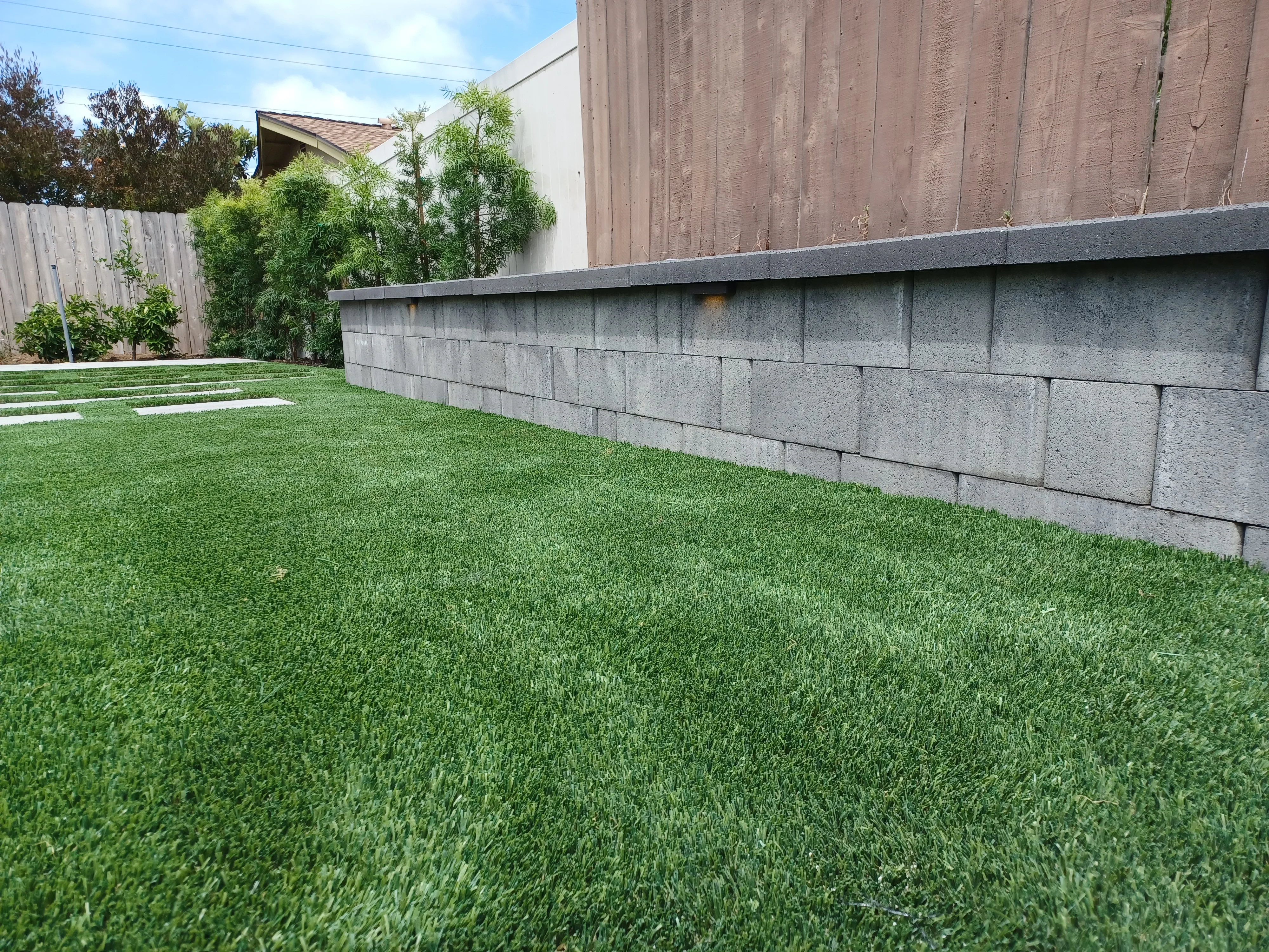 Concrete block retaining wall with synthetic turf lawn and stepping stone pathway
