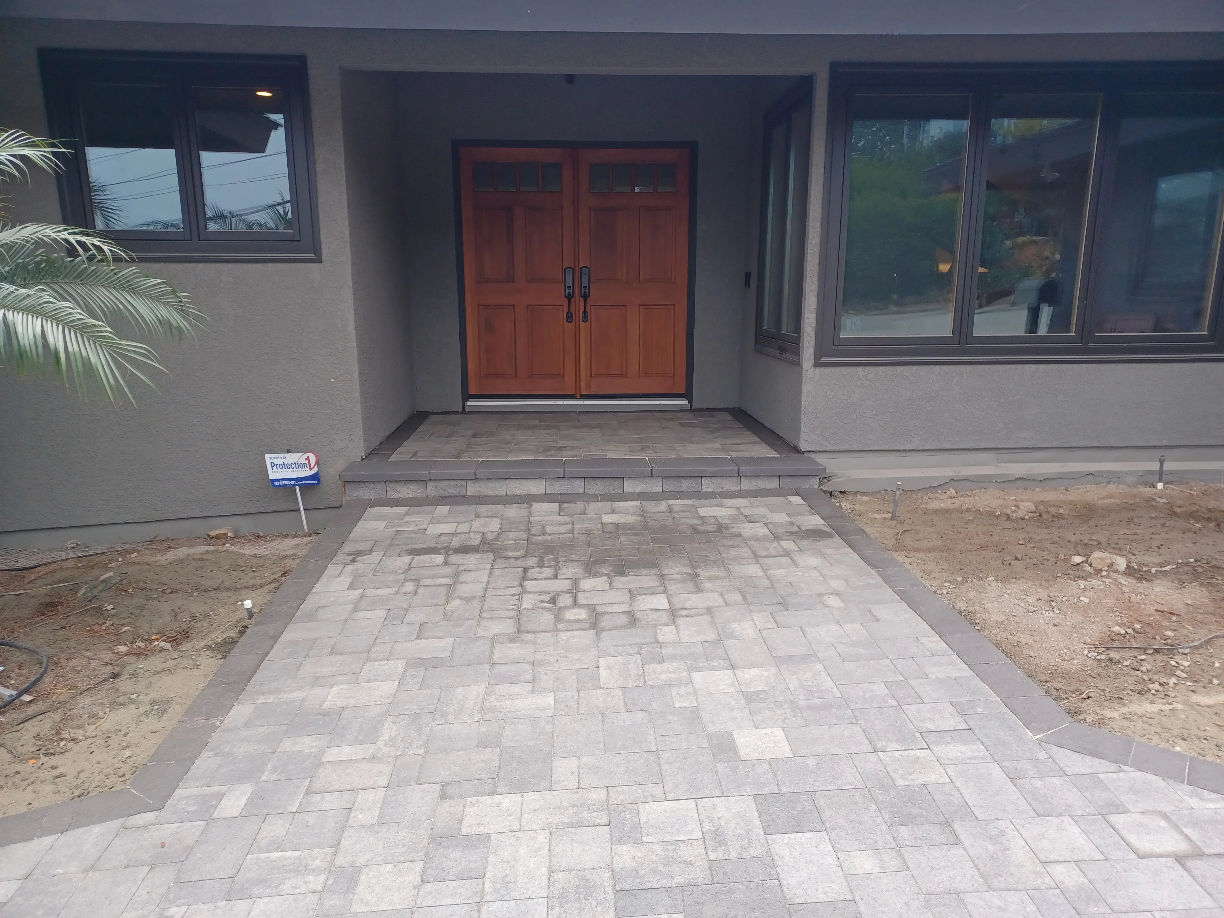 Permeable paver driveway with geometric pattern, gray and tan pavers, raised entry platform with double doors