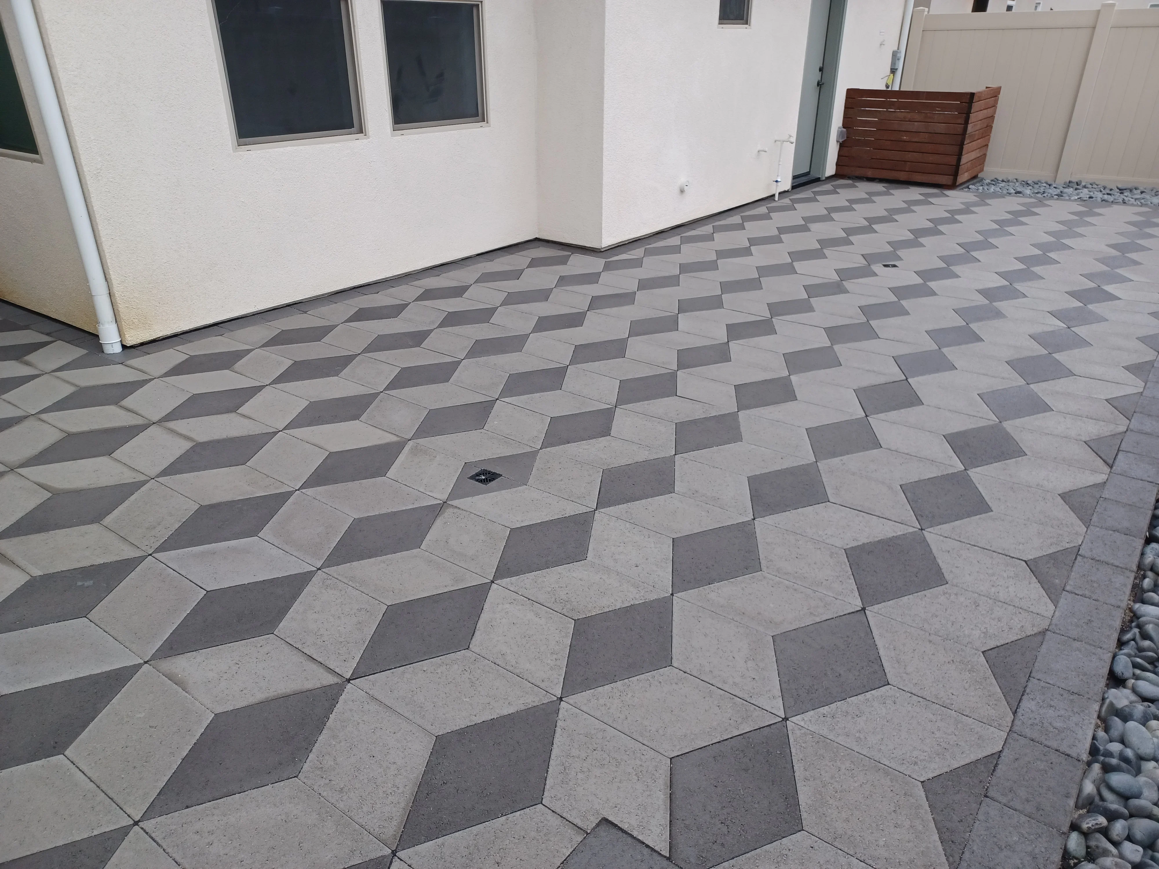 Geometric gray and charcoal concrete paver patio with 3D cube pattern and drainage inlet