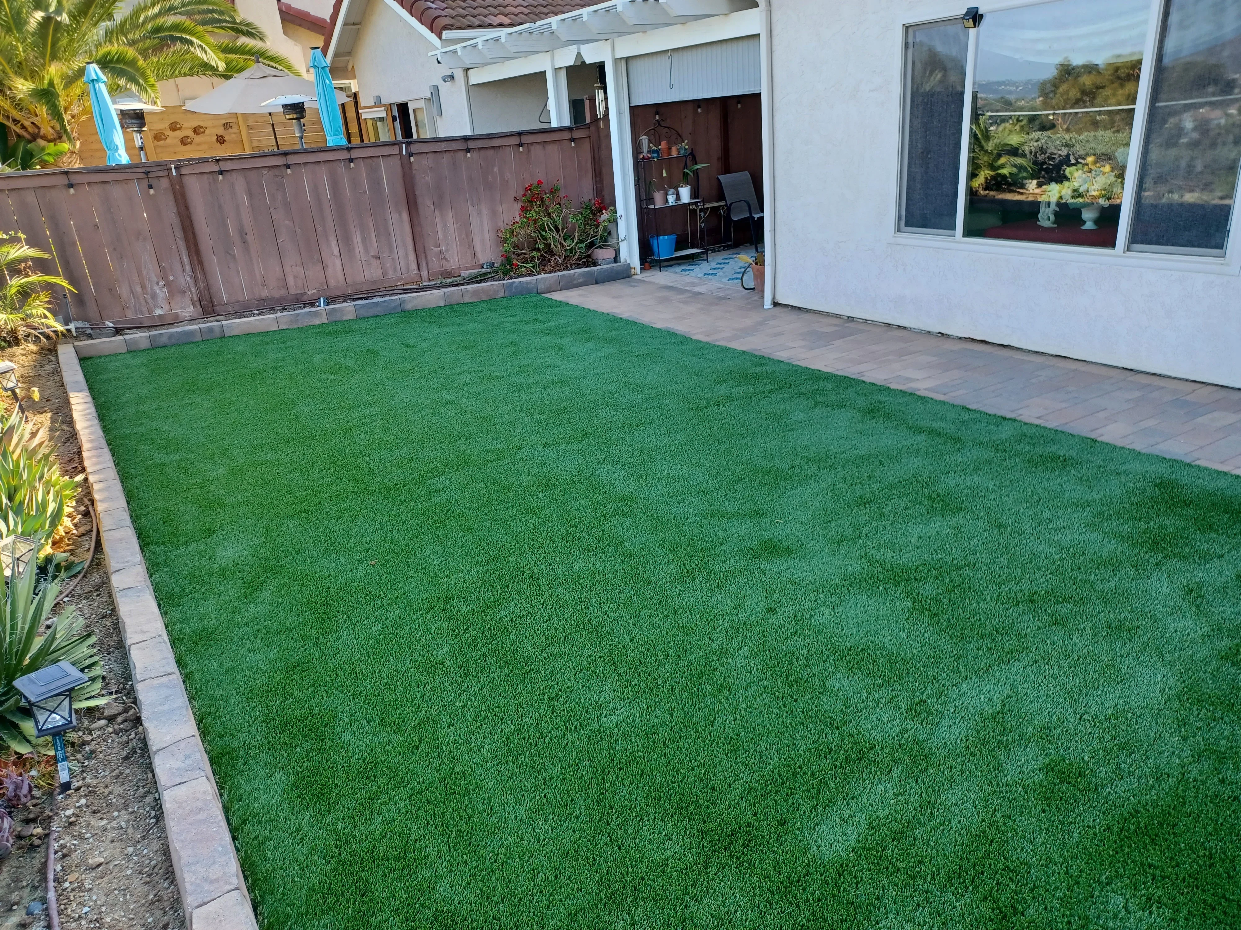 Artificial turf lawn with concrete paver border edging in residential backyard