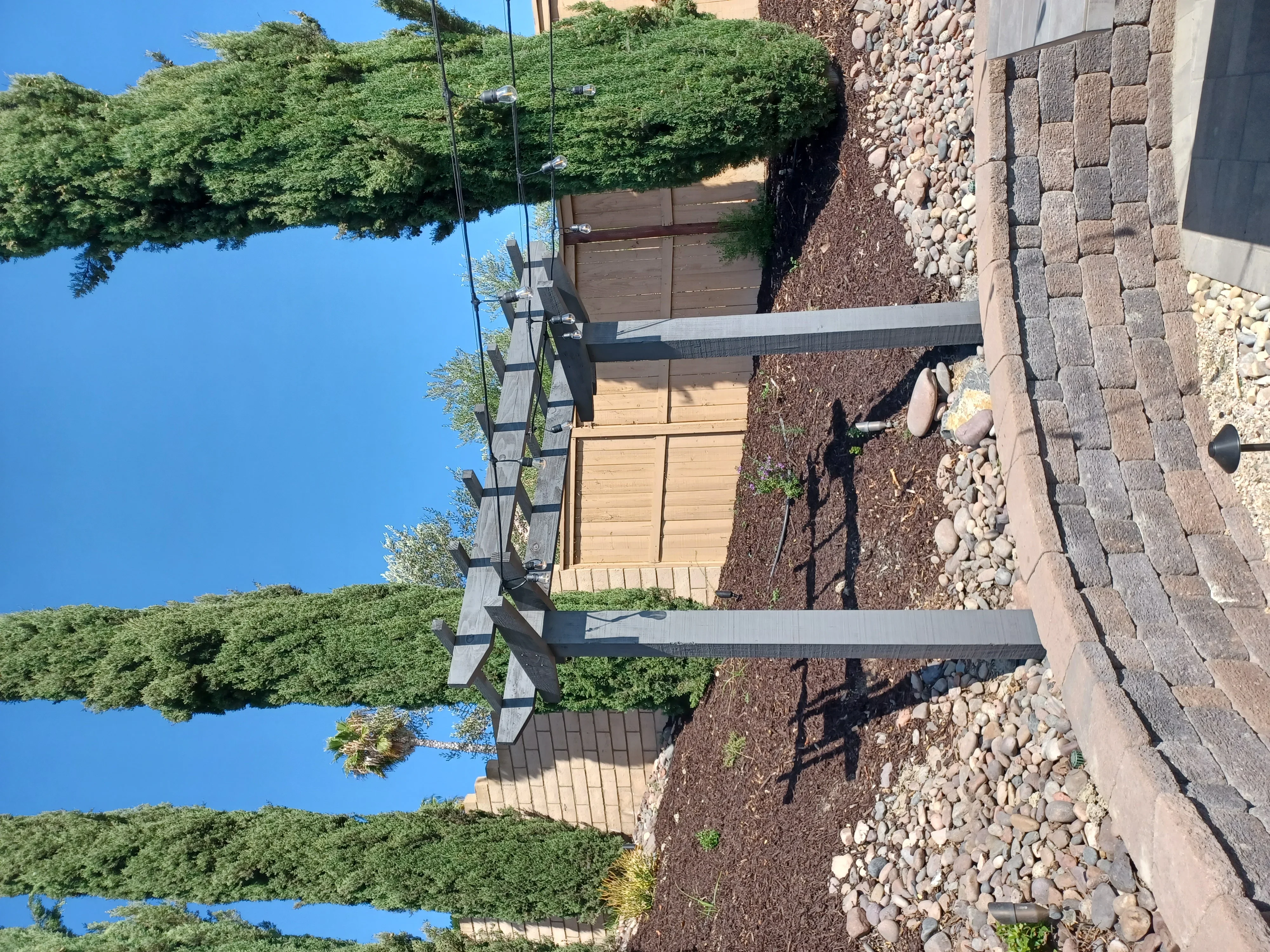 Paver patio with stacked stone retaining wall, river rock base, and mature landscaping