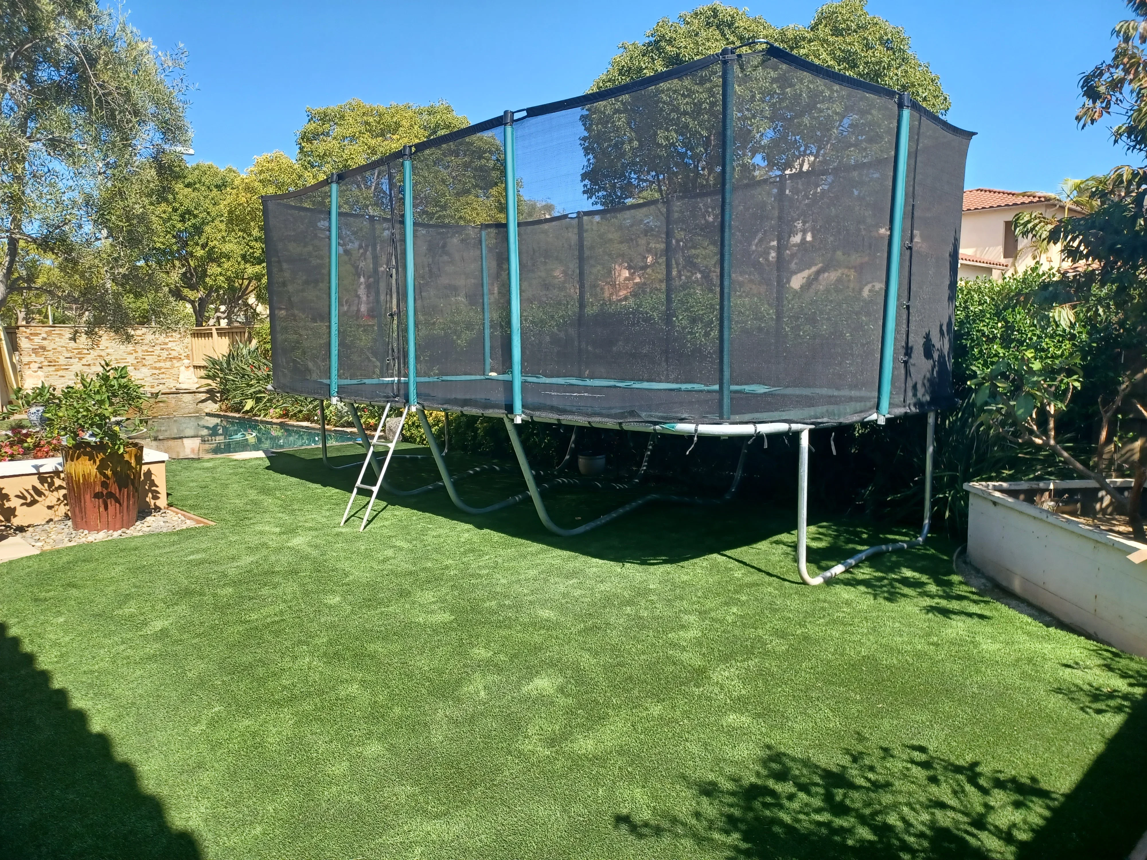 Rectangular trampoline with turquoise frame and dark mesh safety enclosure installed on lawn