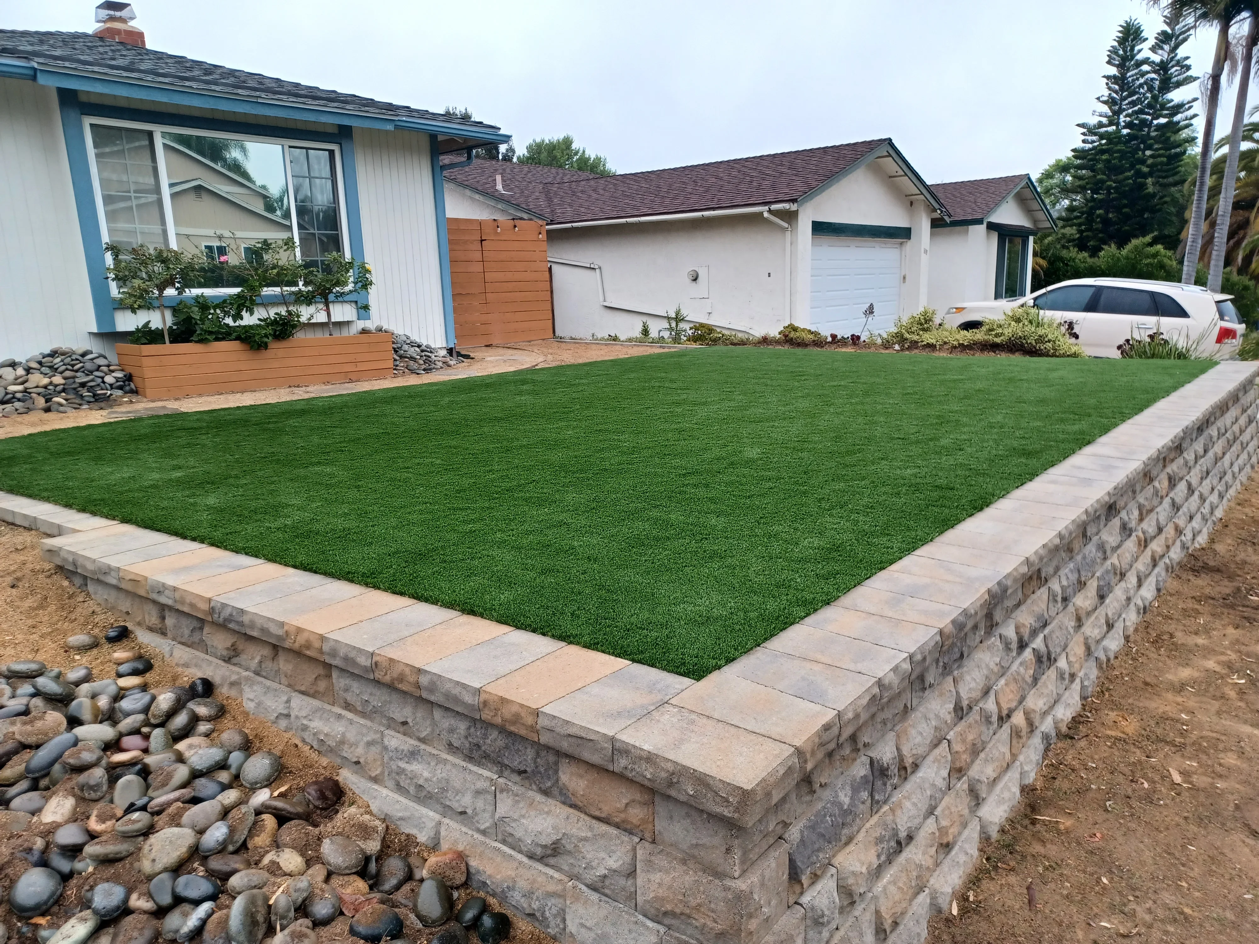 Synthetic turf lawn with concrete block retaining wall and paver edging in front yard