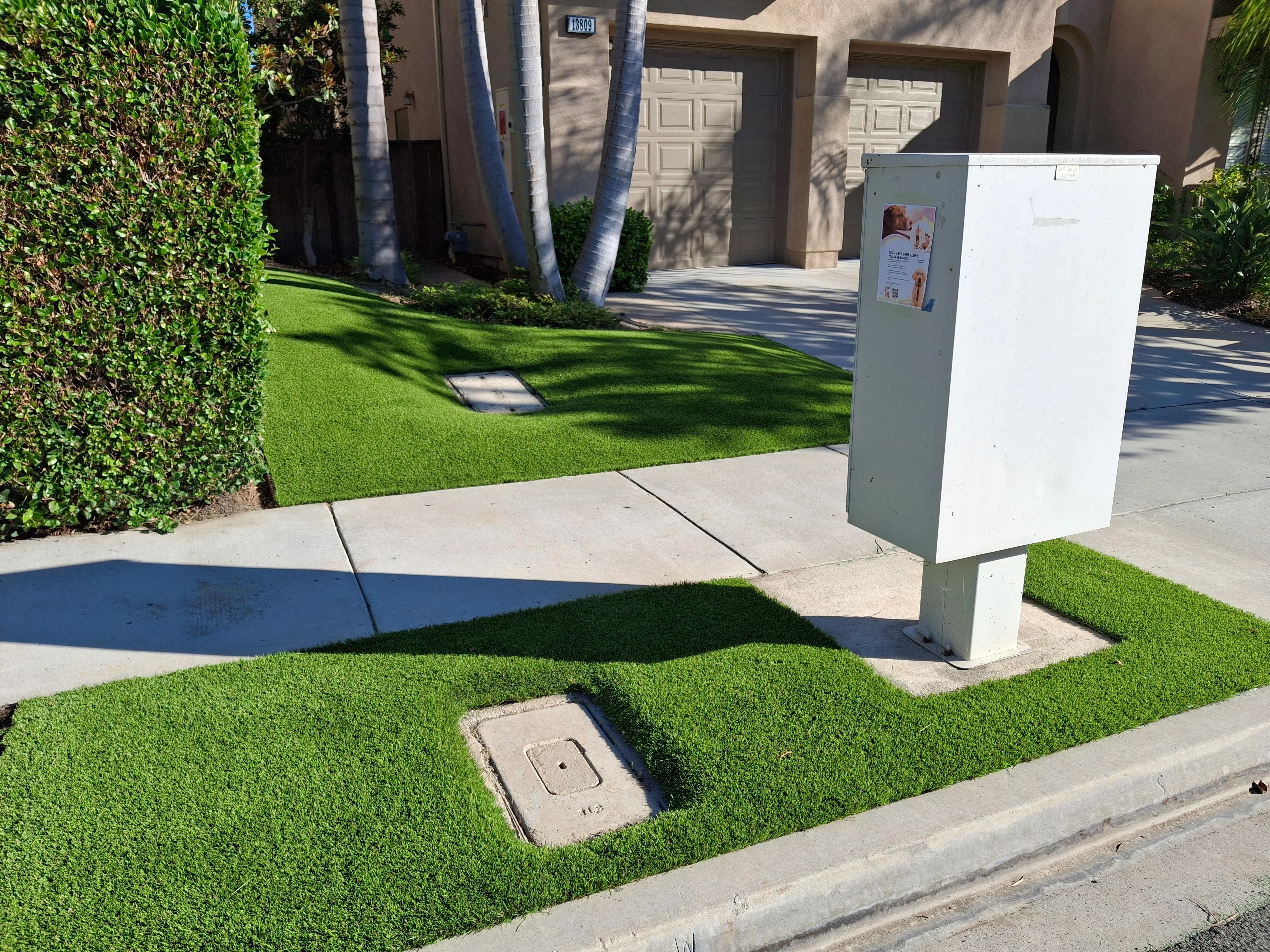 Concrete driveway with control joints, synthetic turf borders, and utility access covers